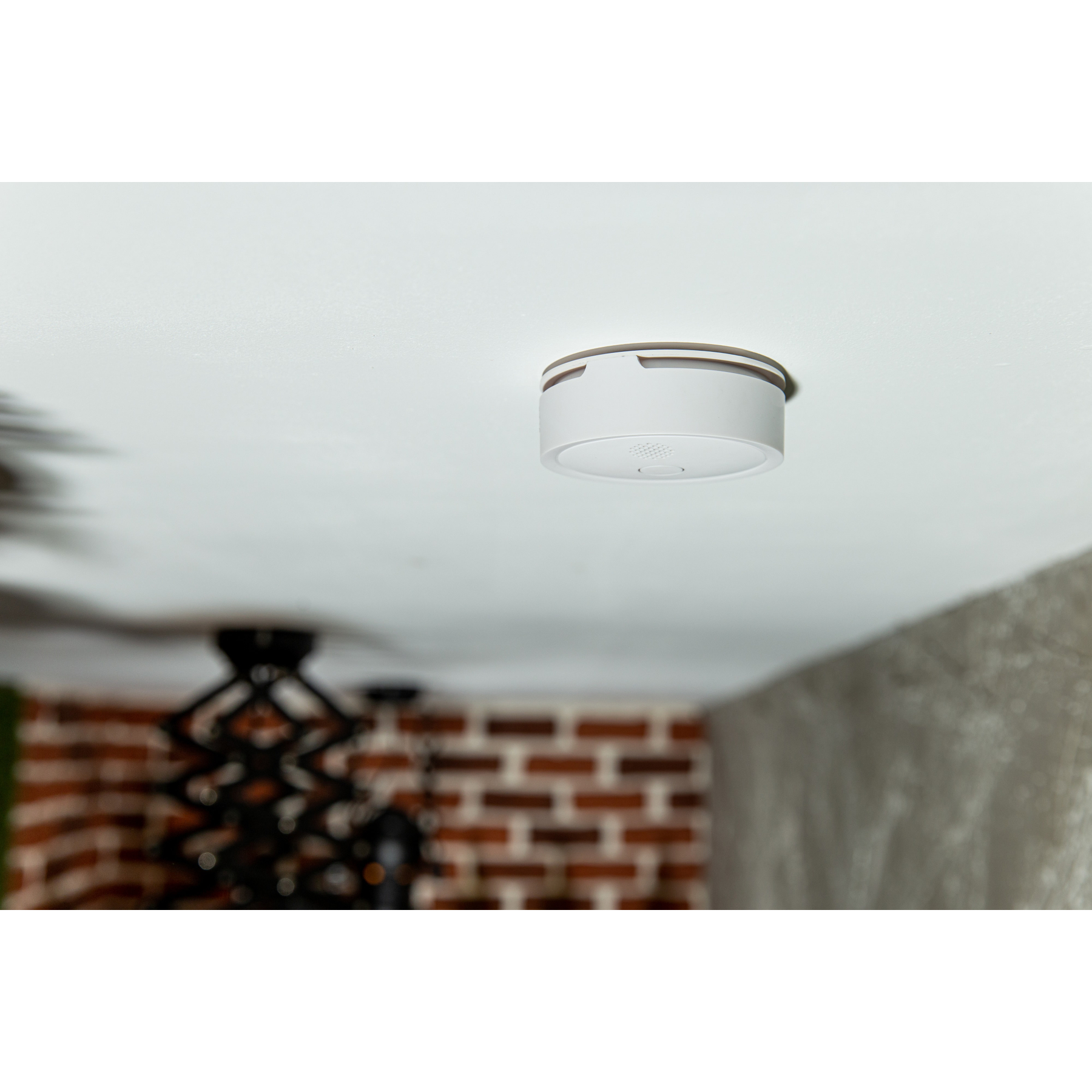 Biały czujnik dymu montowany na suficie w otoczeniu domowym.