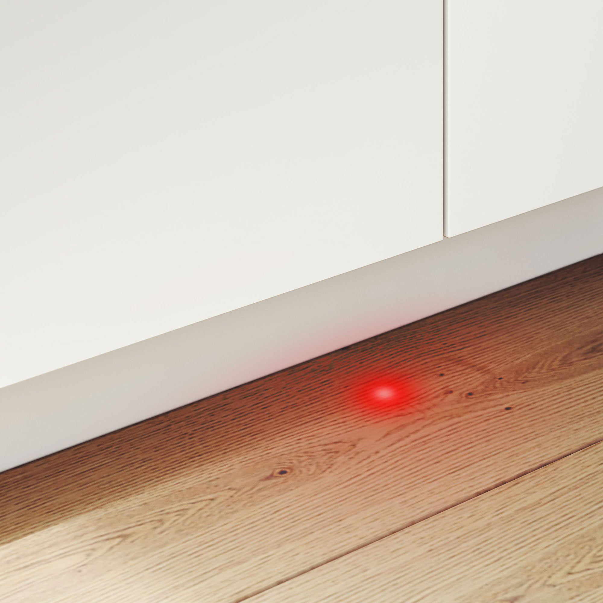 Gros plan sur un mur blanc et une plinthe. Lumière rouge sur un plancher en bois.