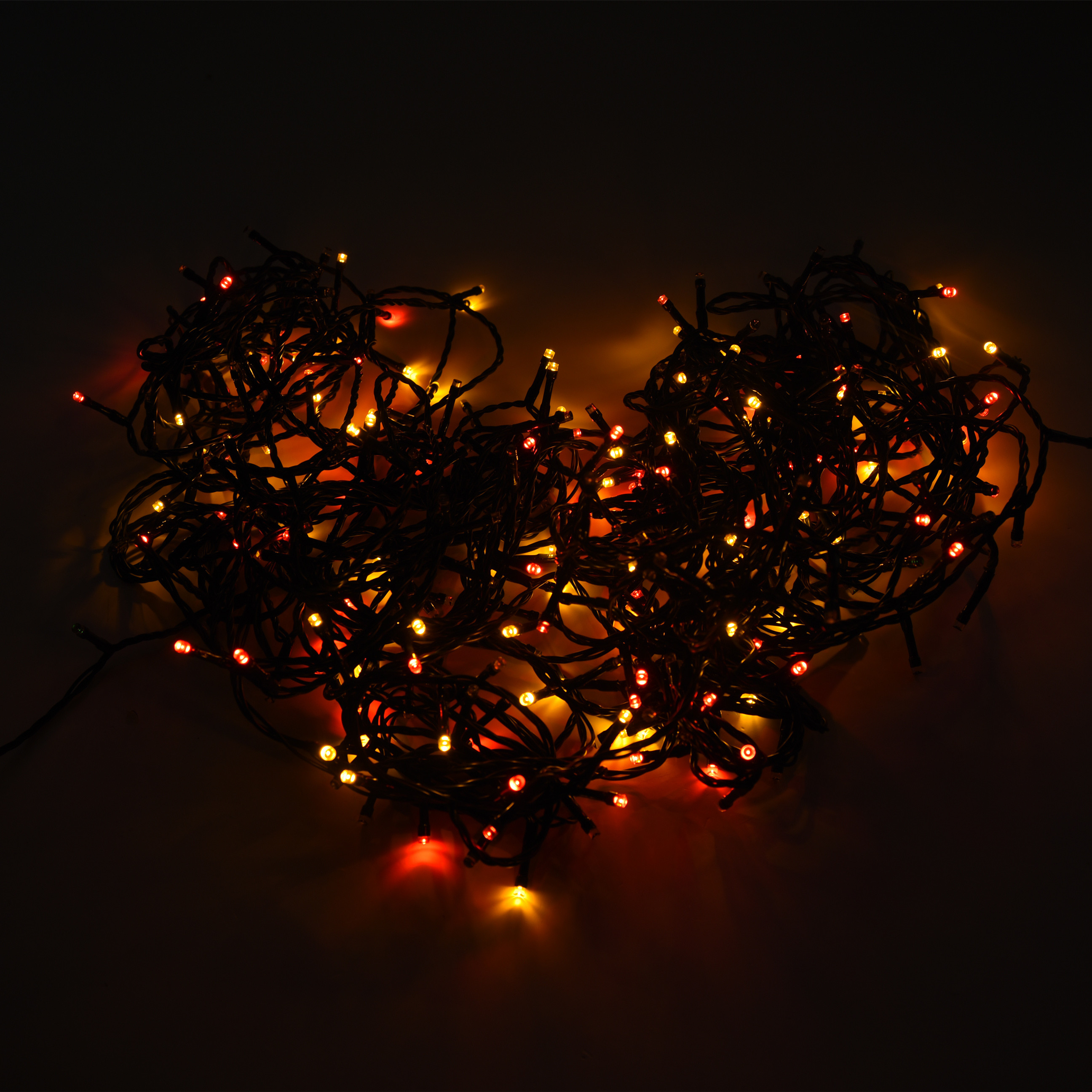 Luci a stringa disposte a forma di cuore, illuminate di rosso e giallo su sfondo scuro.