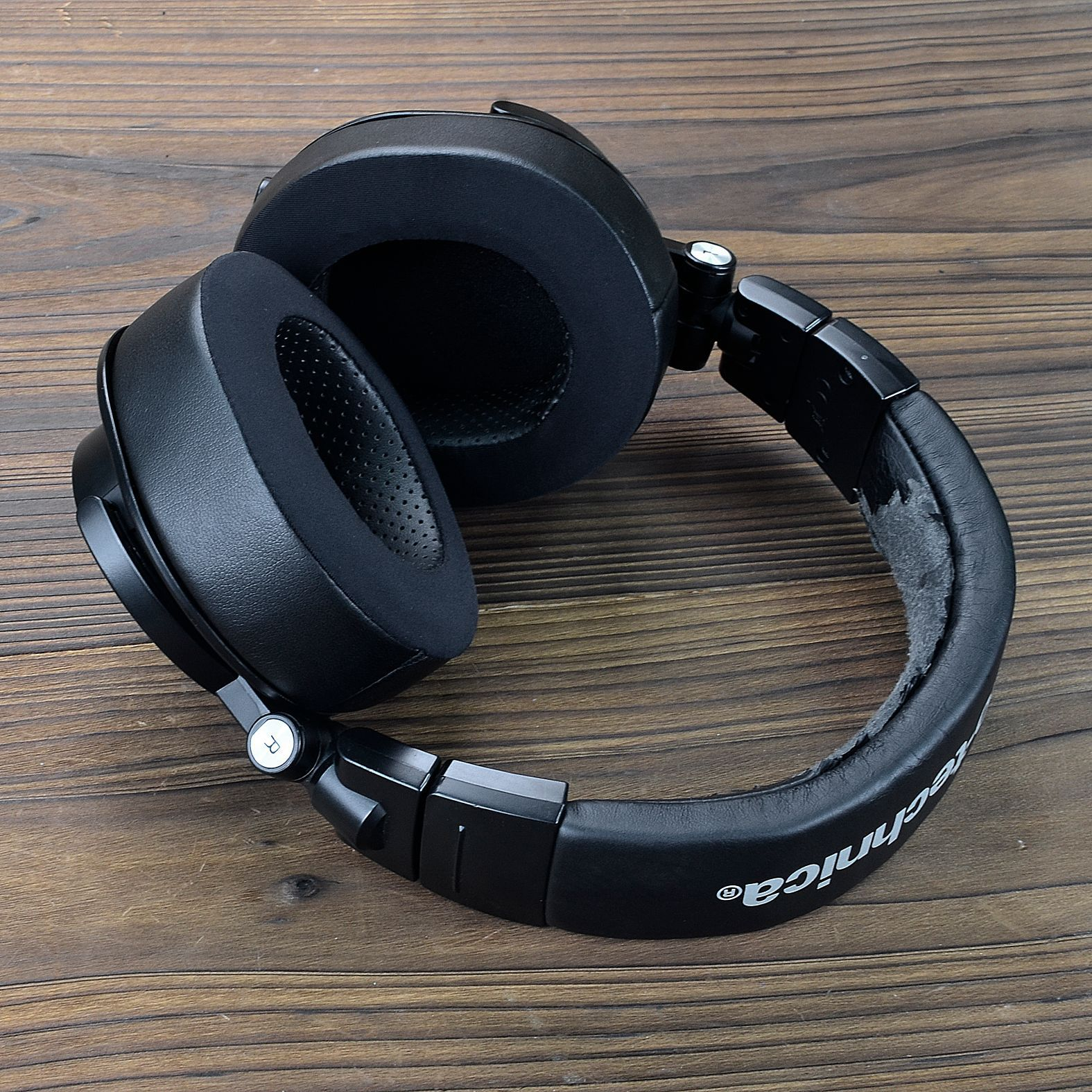Czarne słuchawki nauszne z dużymi nausznicami i pałąkiem, umieszczone na drewnianej powierzchni.