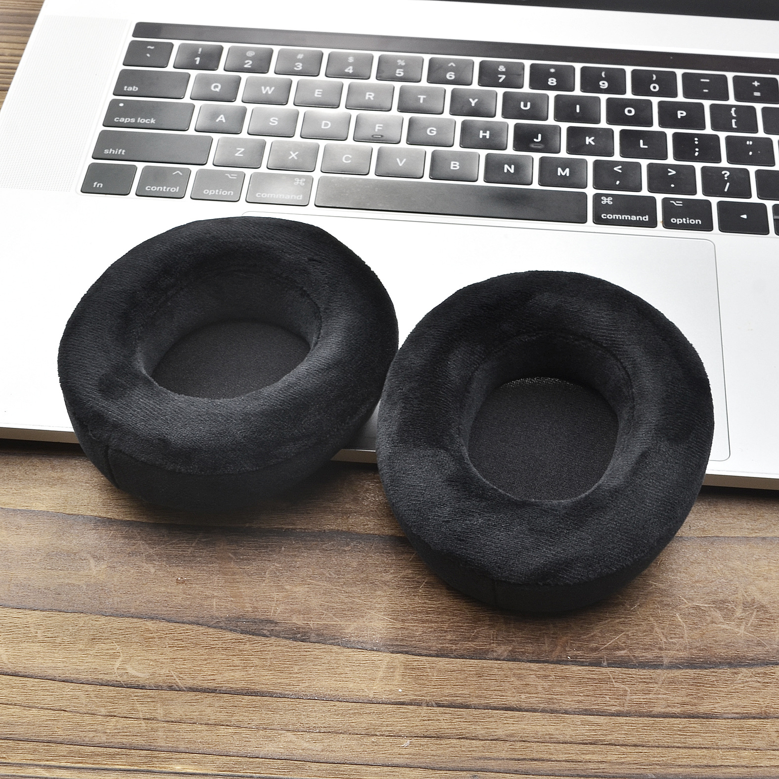 Dwie czarne, pluszowe poduszki na uszy słuchawek na klawiaturze laptopa, na drewnie.