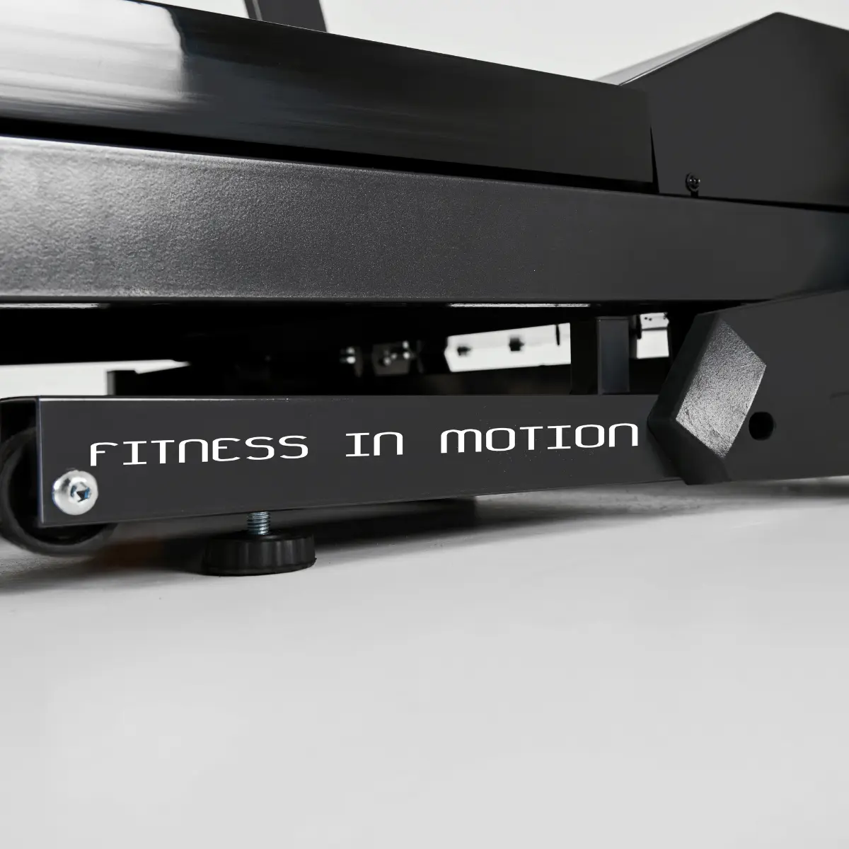 The bottom part of a black treadmill with the words 'FITNESS IN MOTION' in white on a silver bar.