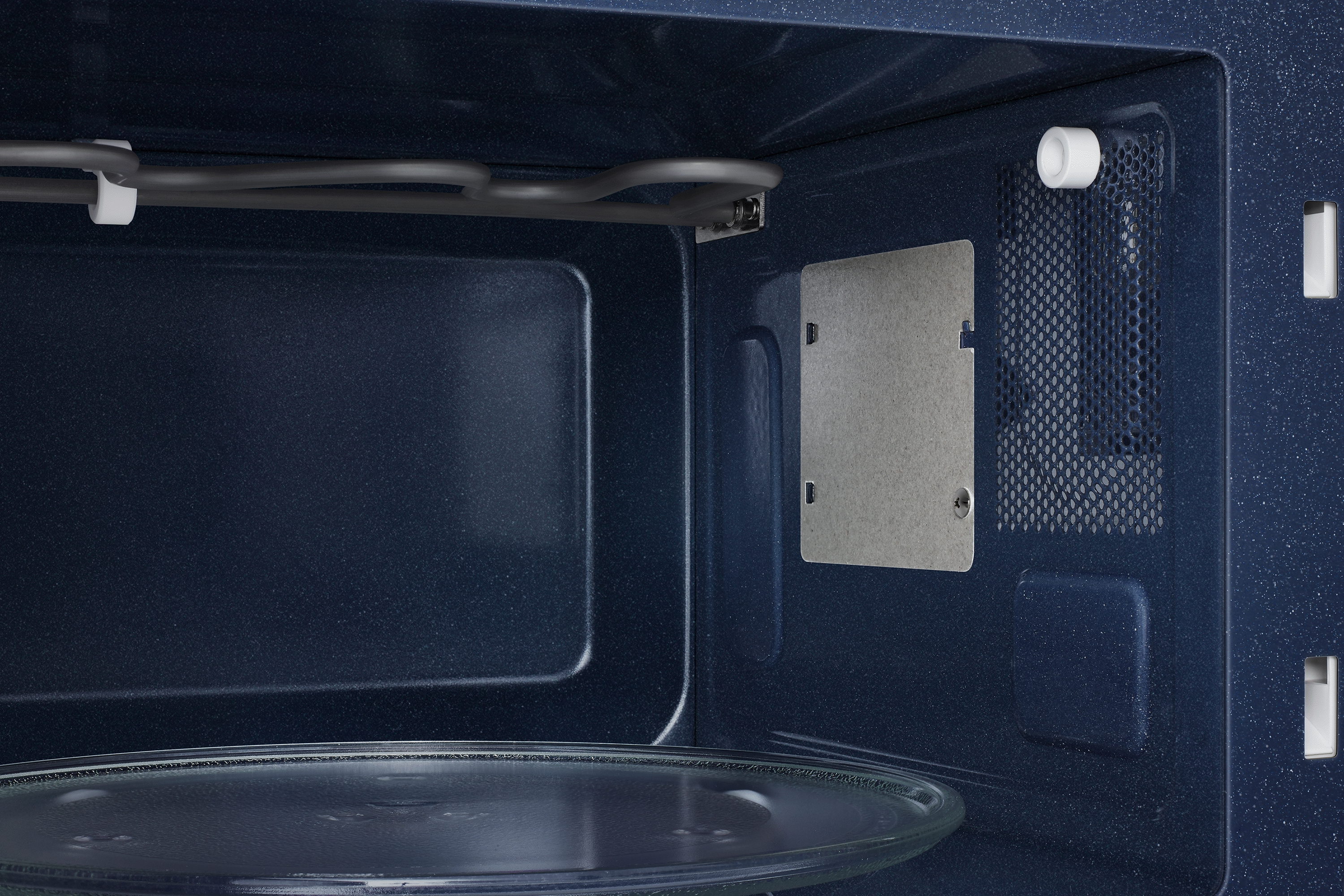 All'interno di un microonde blu scuro. Sono visibili il piatto in vetro e un elemento riscaldante. Lo sfondo è blu scuro.