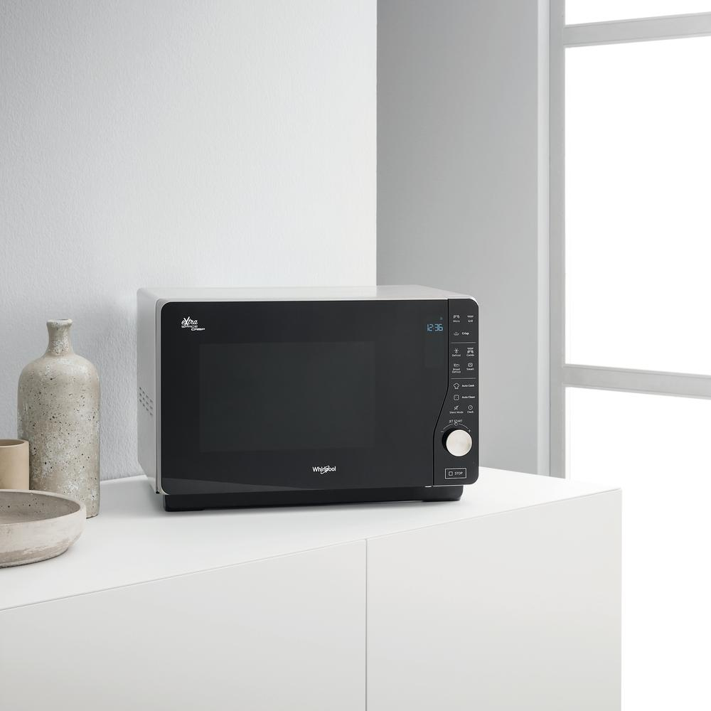 Czarna kuchenka mikrofalowa na białej powierzchni. Posiada wyświetlacz cyfrowy i przyciski sterowania, z oknem.