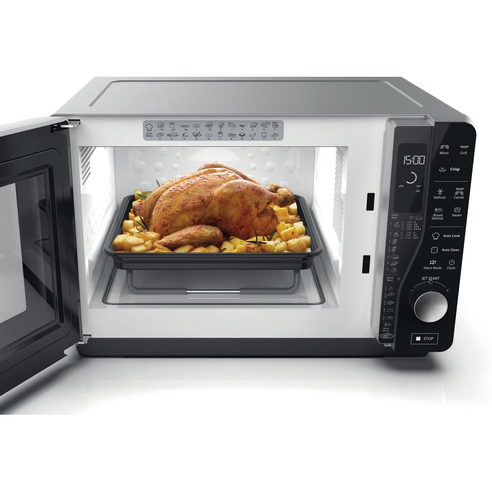 Kuchenka mikrofalowa z pieczonym kurczakiem i ziemniakami na czarnej tacy.