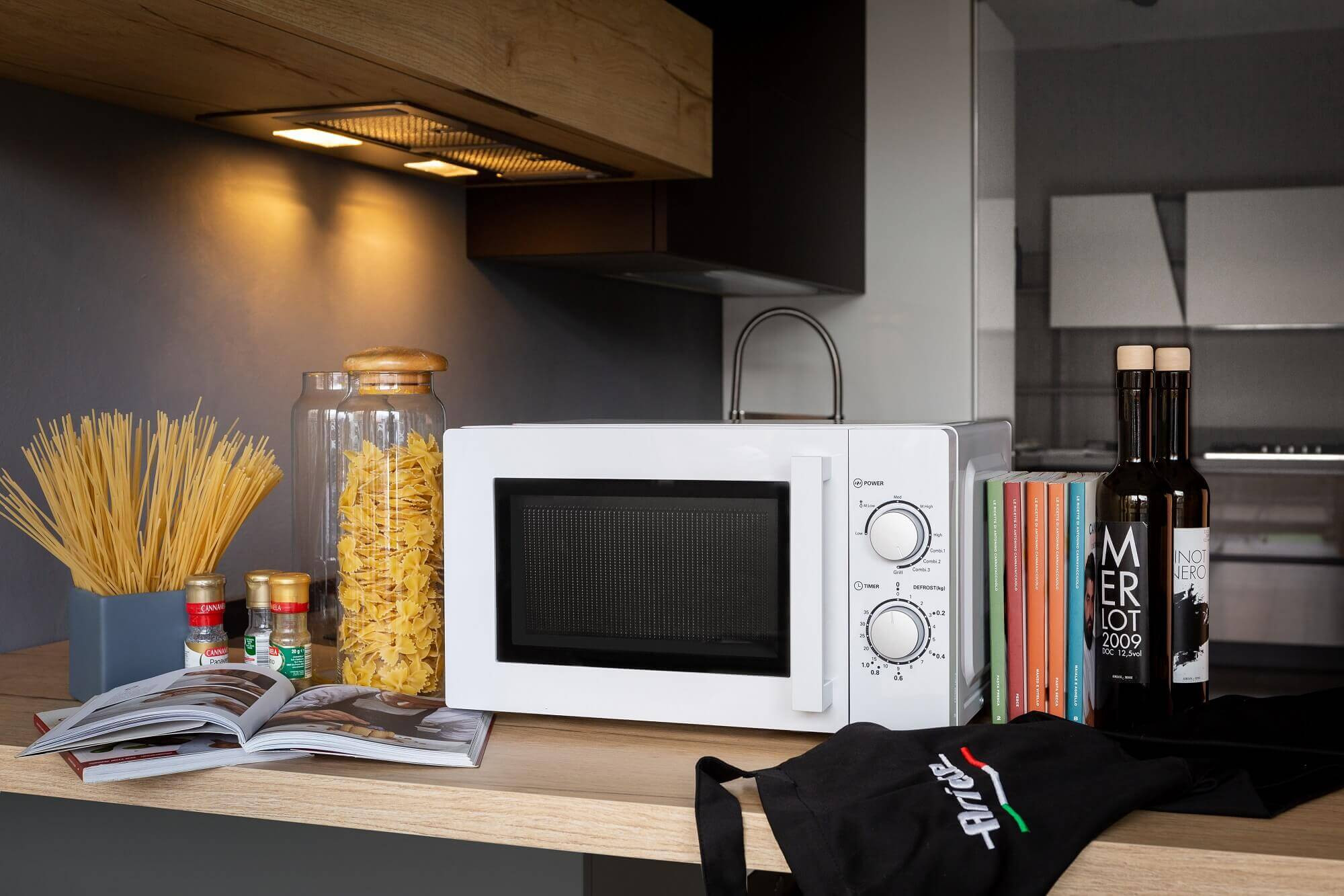 Witte magnetron op een houten aanrecht met eten, kruiden en flessen in de buurt.