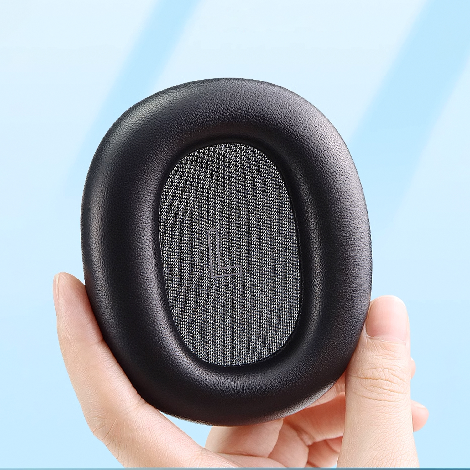 Zbliżenie czarnej poduszki nausznej do słuchawek trzymanej przez dłoń.