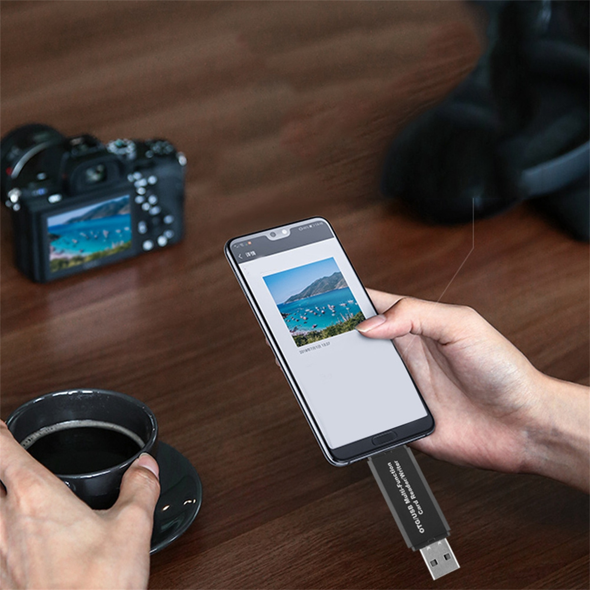 Eine Person hält ein Telefon mit einem Foto einer Bucht, verbunden mit einem USB-Adapter. Kamera und Kaffeetasse in der Nähe.