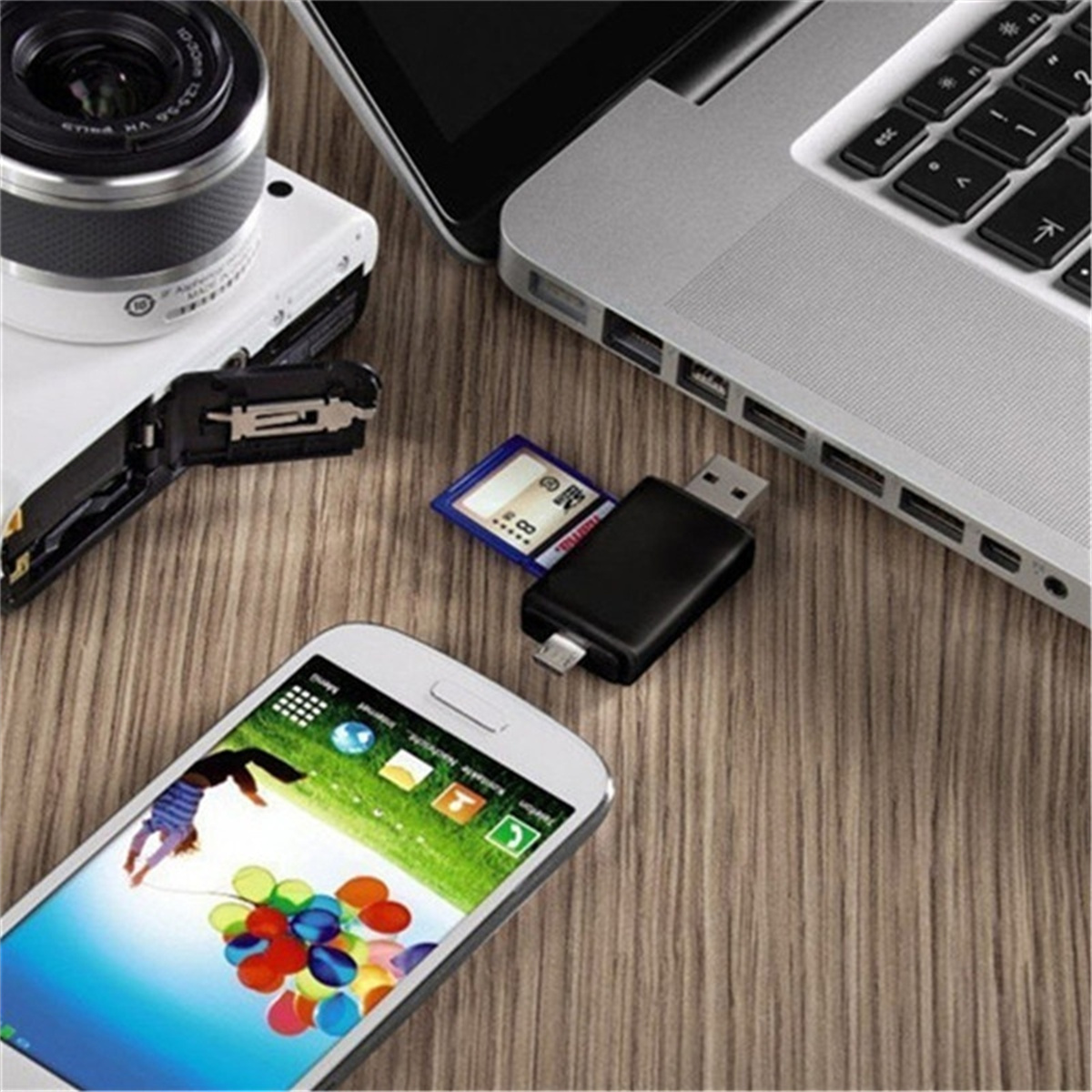 Eine Kamera, ein Laptop, ein Telefon, eine SD-Karte und ein USB-Adapter liegen auf einer Holzoberfläche.