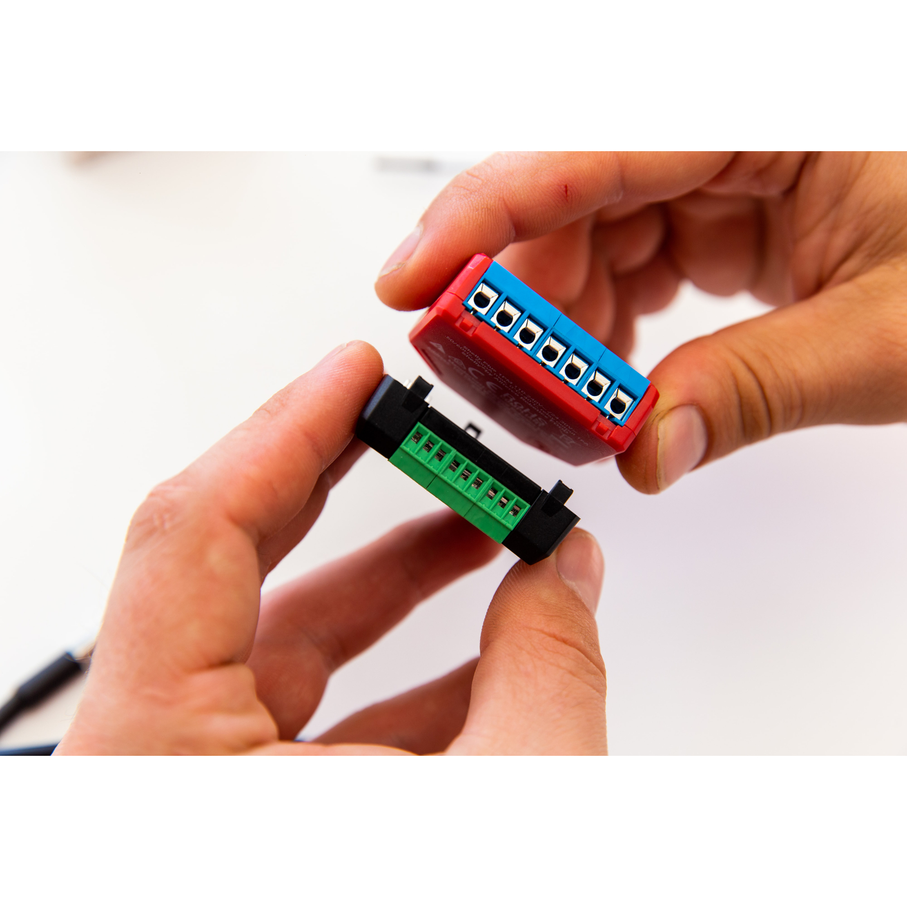 Dos manos sosteniendo conectores eléctricos rojos y verdes. Los conectores están uno al lado del otro.