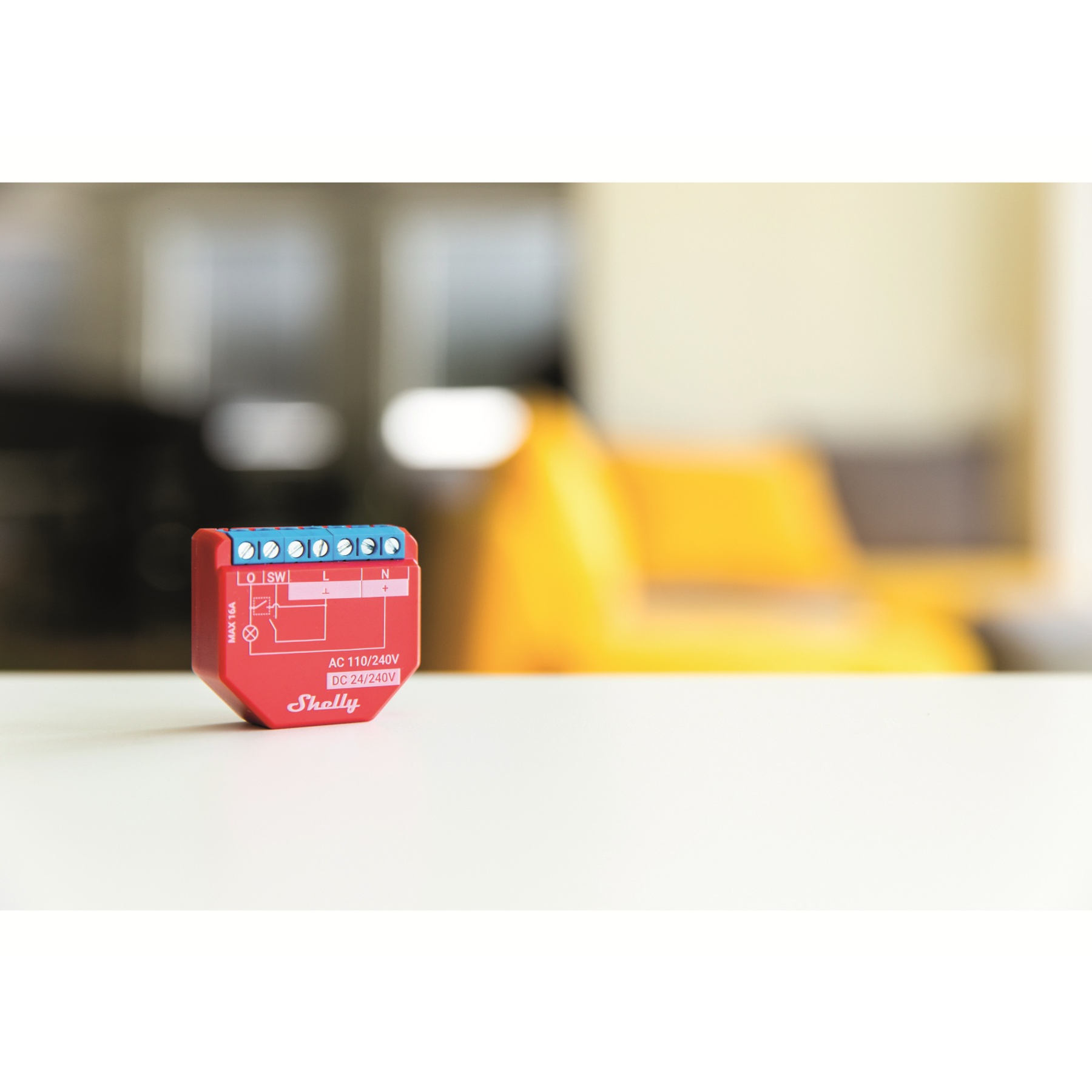 Ein rotes Smart-Home-Gerät. Es hat Klemmen und ein Etikett oben. Der Hintergrund ist unscharf.