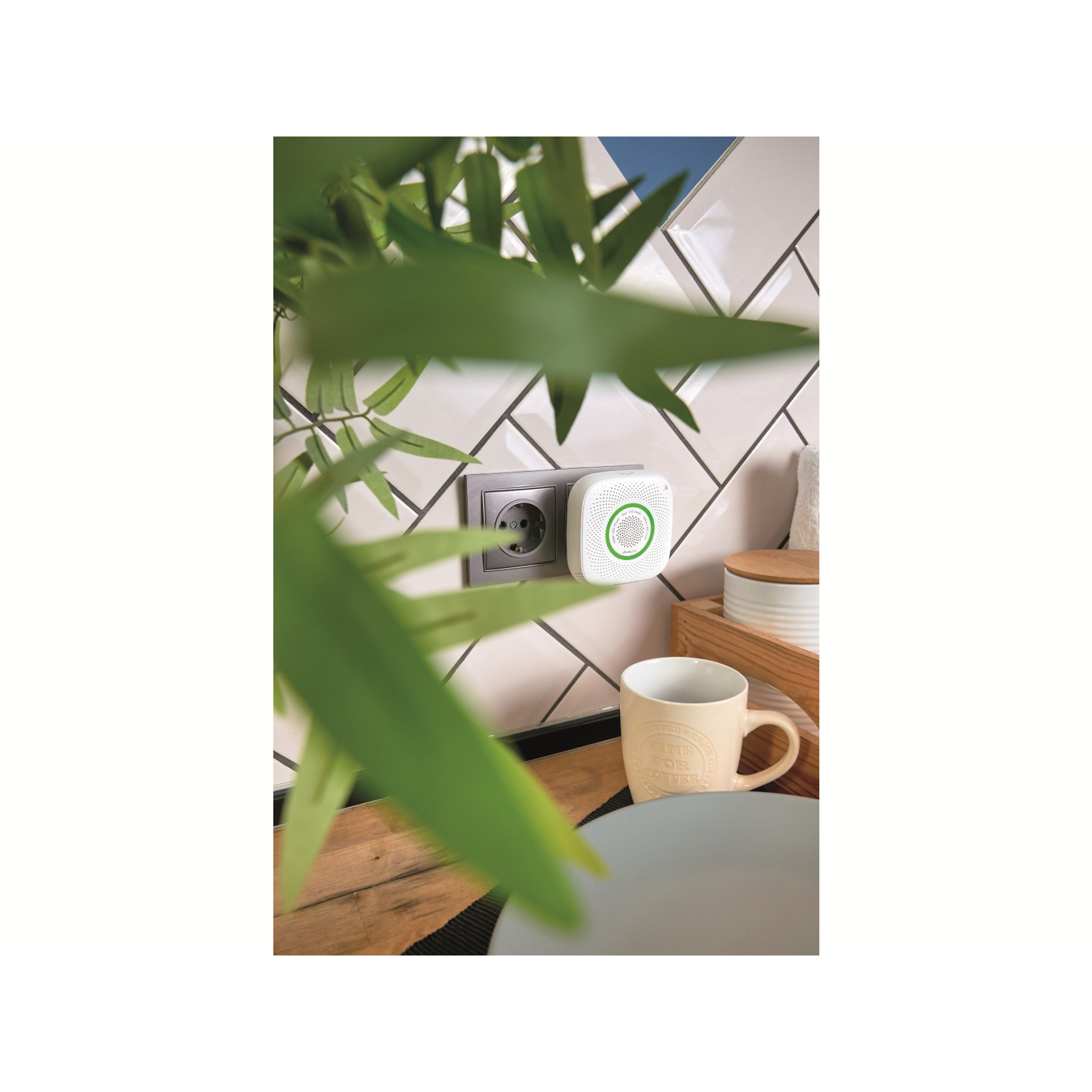 Biały czujnik dymu na ścianie z wtyczką. Kubek kawy na drewnianej powierzchni.