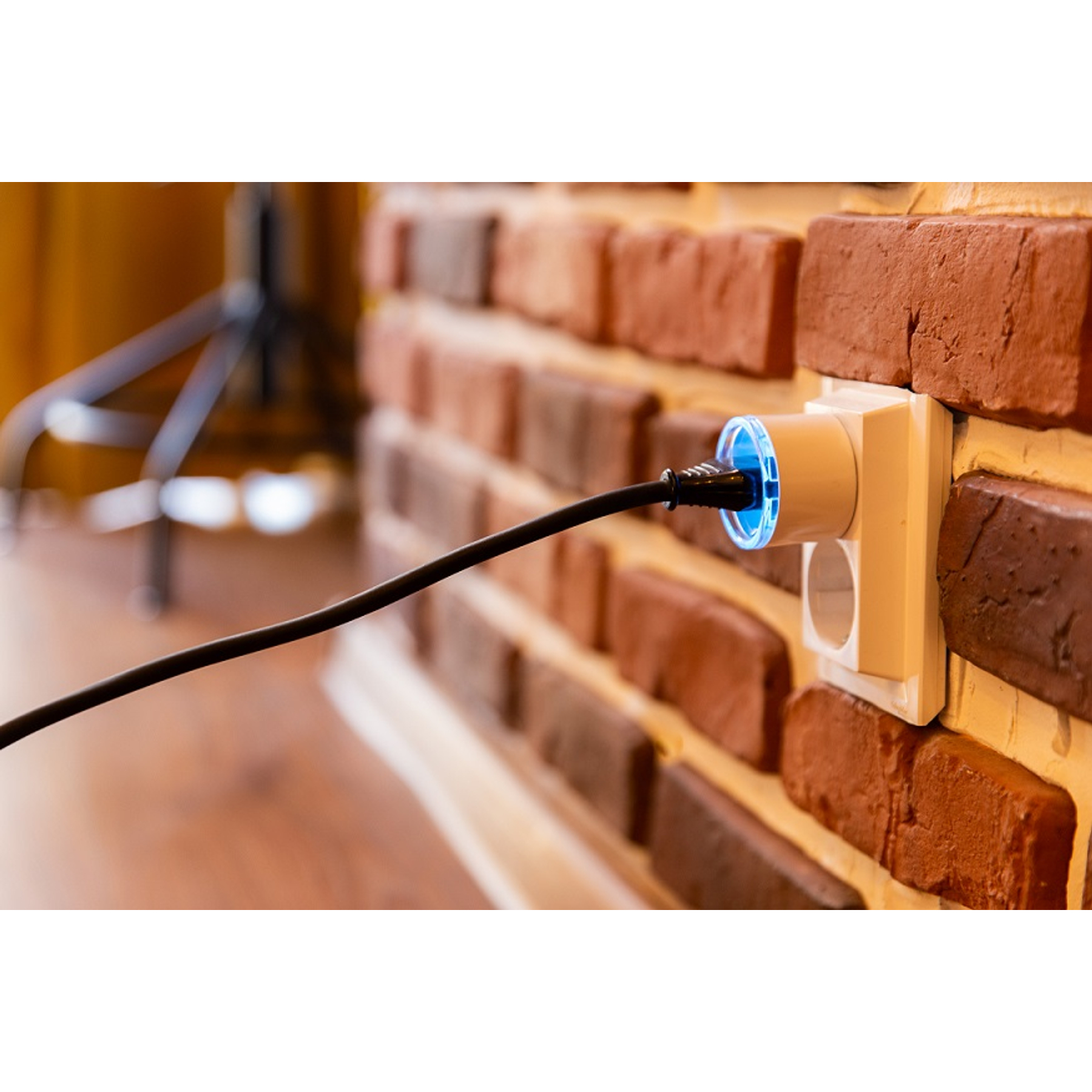 Un enchufe conectado a una pared de ladrillo con un cable negro.