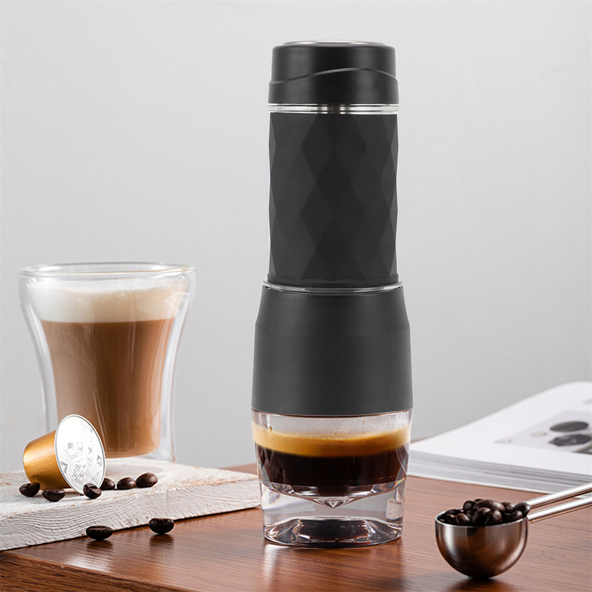 Schwarzer Espressomaschine mit einem Glas Espresso. Kaffeebohnen und ein Löffel auf dem Tisch.