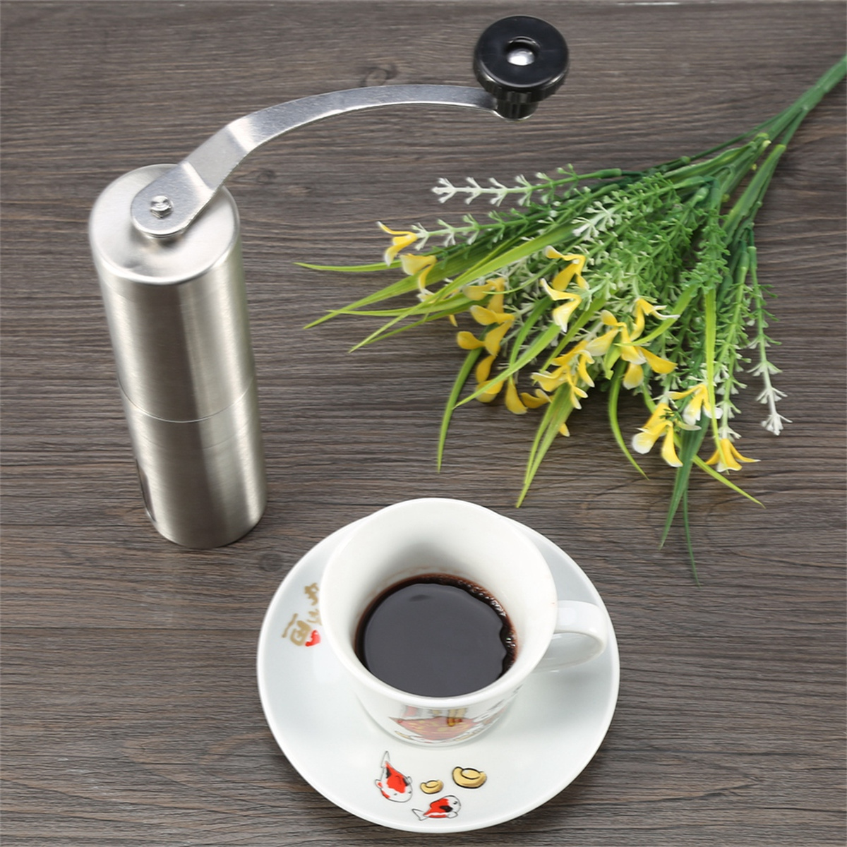 Eine manuelle Kaffeemühle und eine Tasse Kaffee mit gelben Blumen auf einer Holzoberfläche.