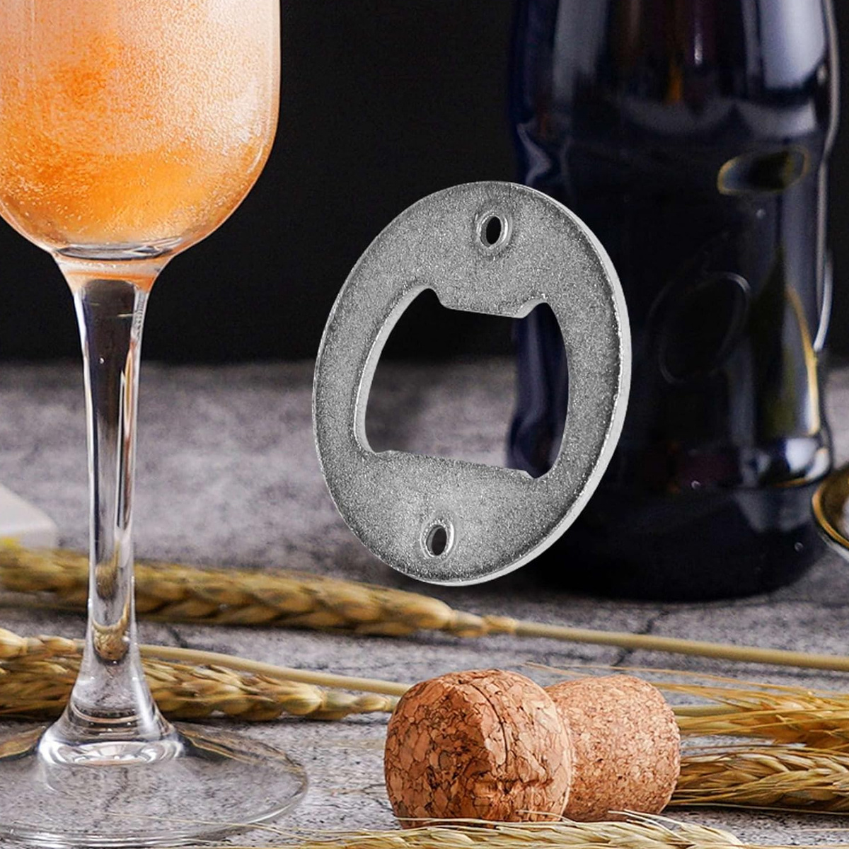 Ein Metall-Flaschenöffner, der auf einer Oberfläche mit Weizen und Korken liegt, neben einem Weinglas mit einem Orangendrink.