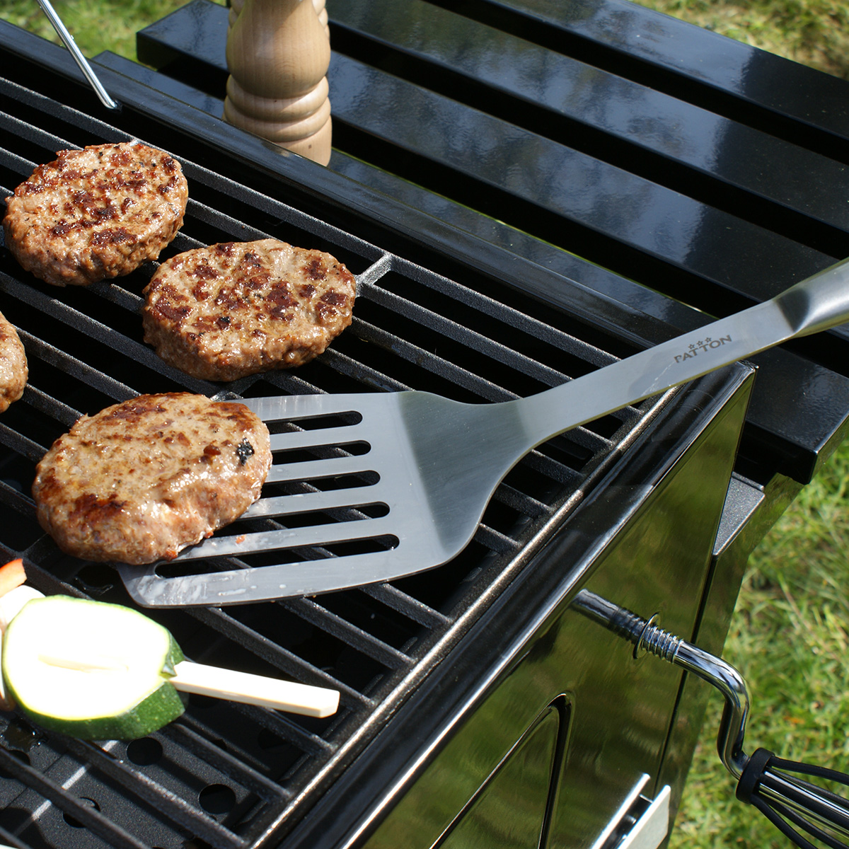 A grill with cooked burgers. A spatula is resting on the grill next to the burgers.