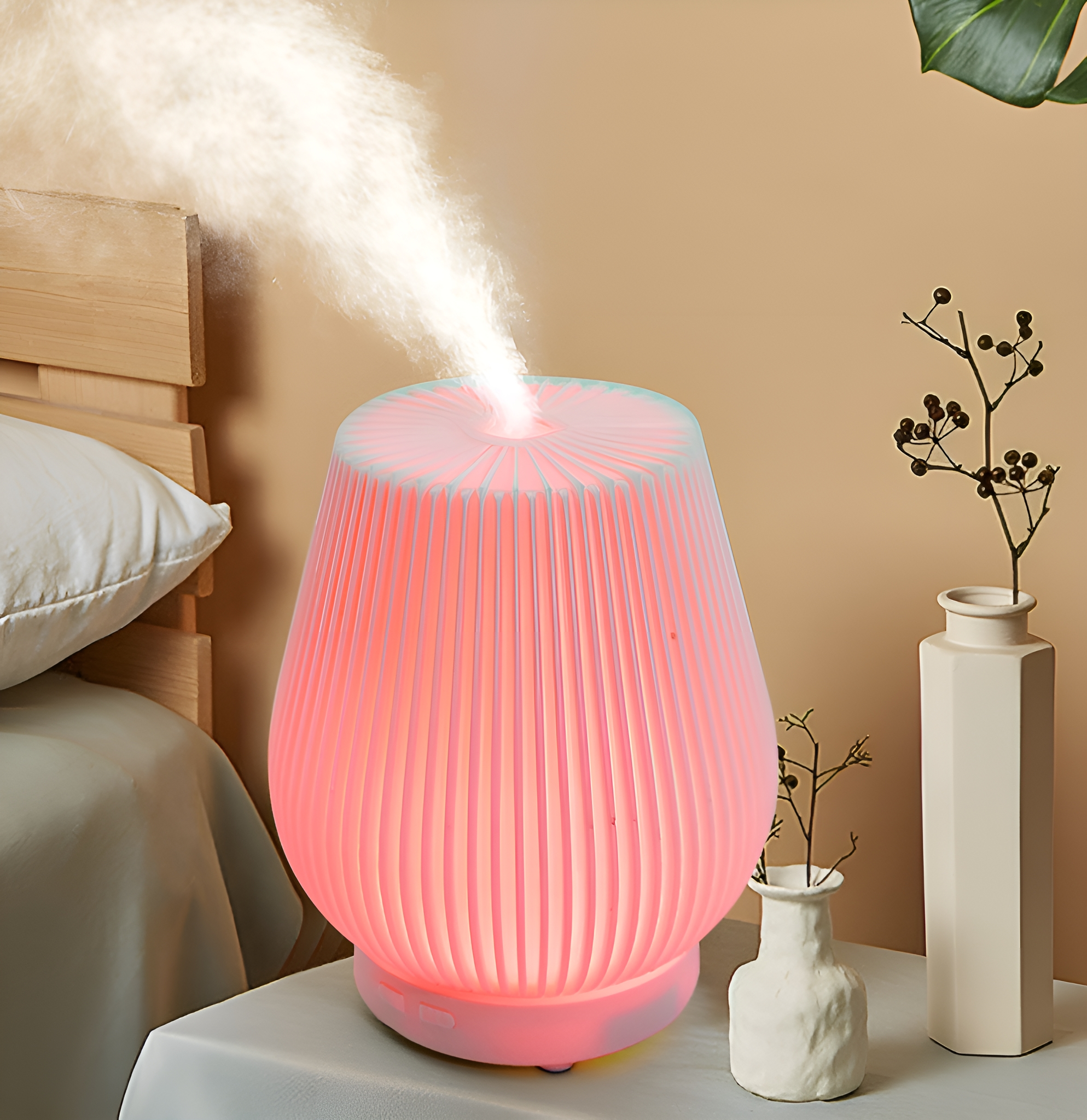 Ein rosa-weißer Luftbefeuchter auf einem Tisch, mit Nebel, der herauskommt. Rechts eine Vase und Pflanze.