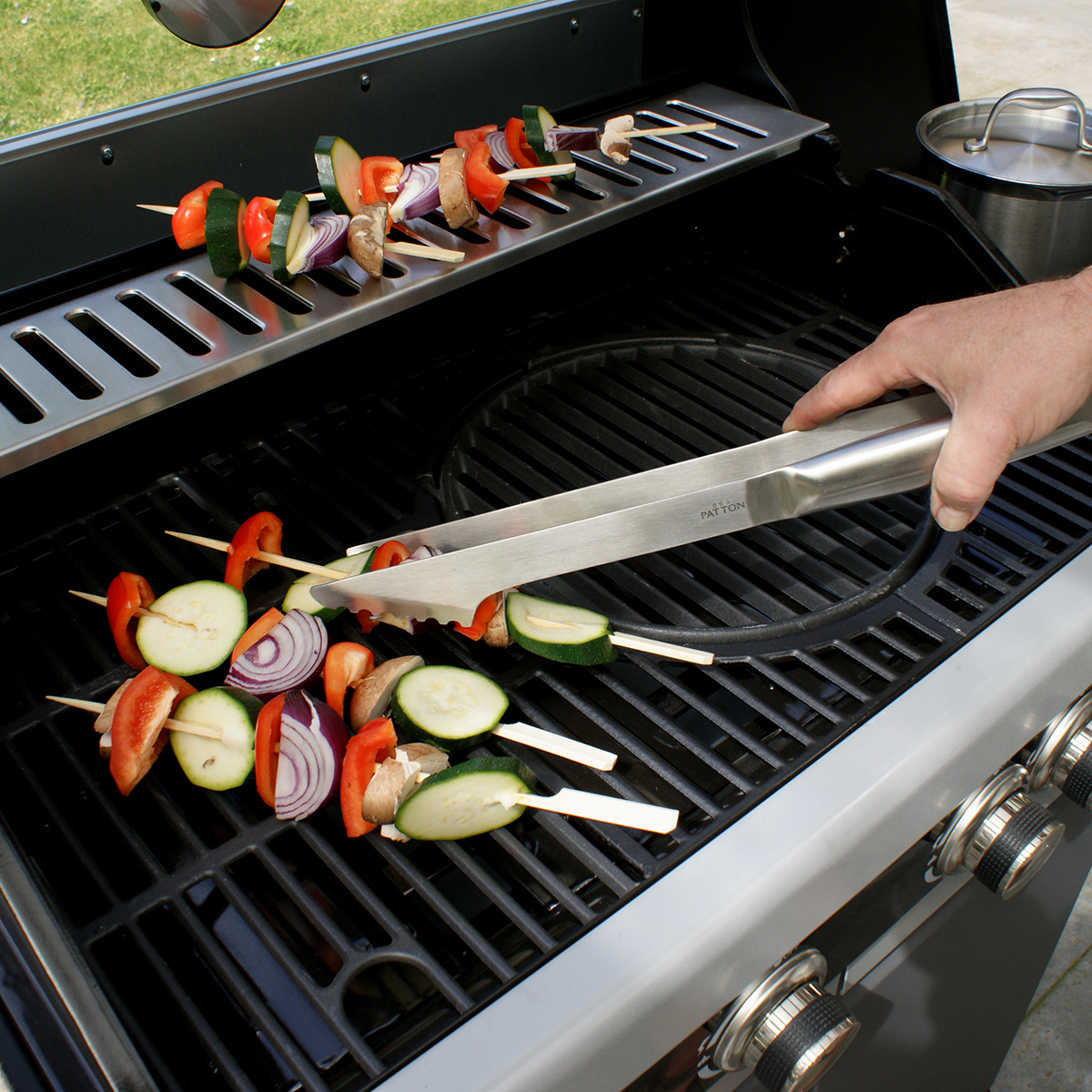 A person grilling skewers of vegetables and meat on a grill.