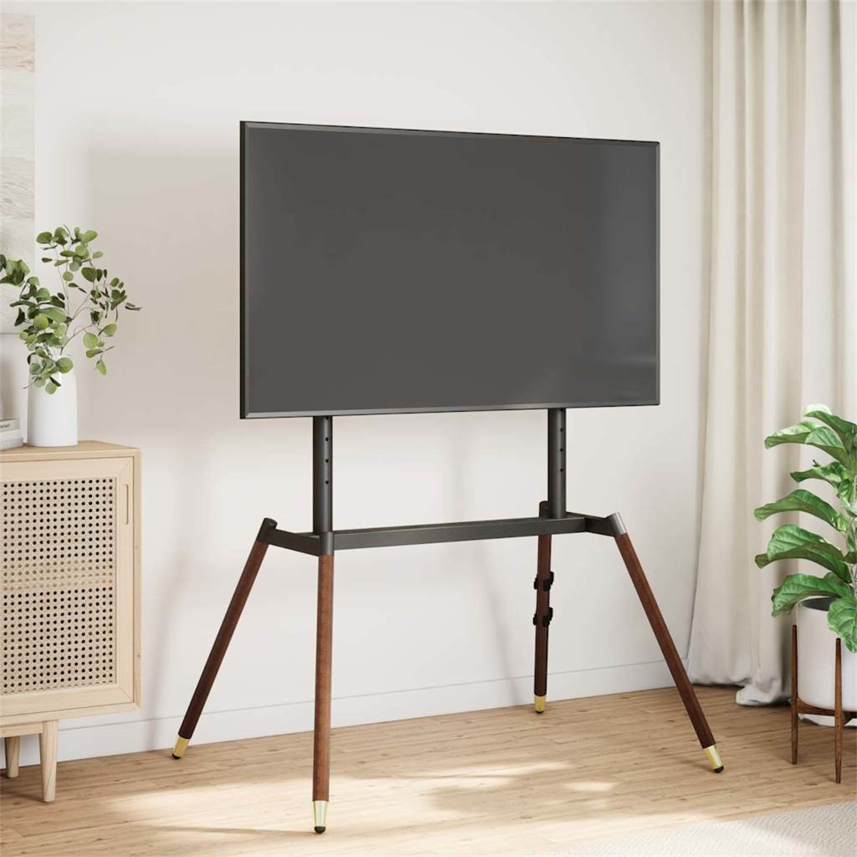 Ein Fernseher auf einem Ständer mit Holzsockel und Beinen, eine weiße Wand und eine Pflanze.