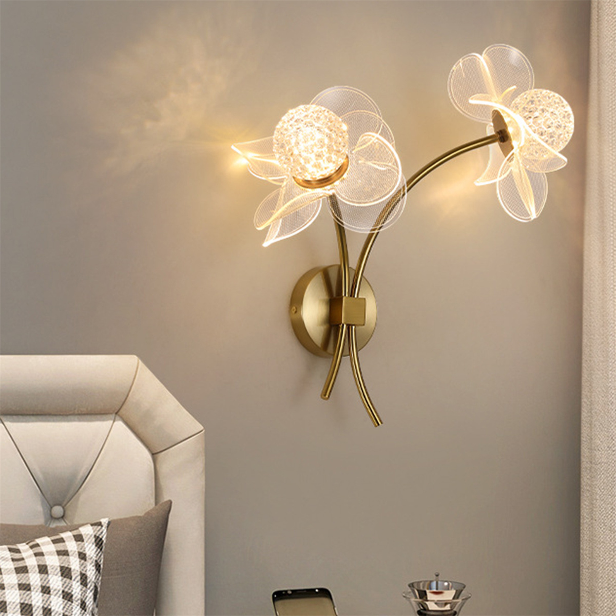 Wandleuchte mit floralem Design, goldfarbenem Sockel und warmer Beleuchtung.