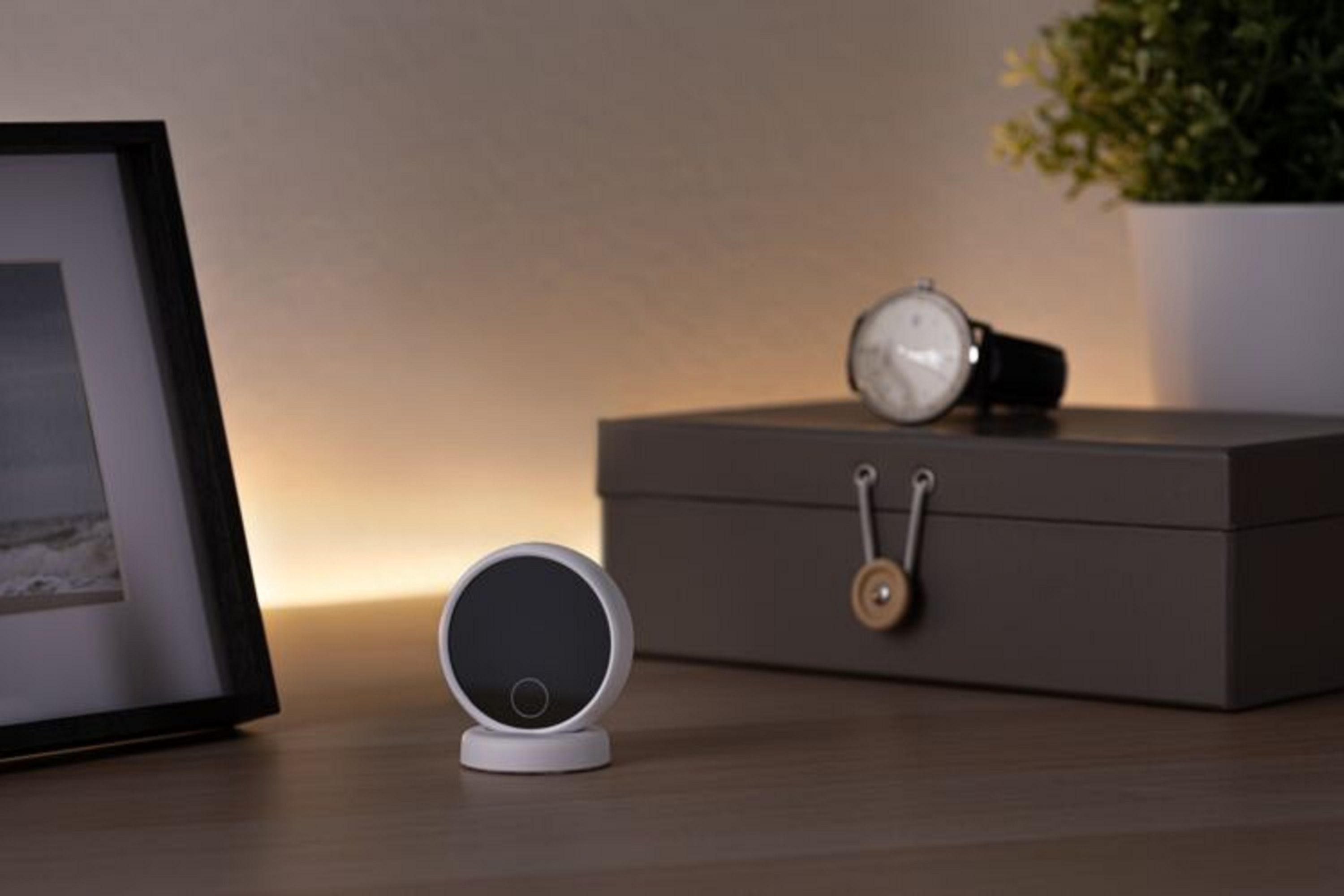 Mała biała kamera bezpieczeństwa na drewnianym stole z zegarkiem i rośliną.