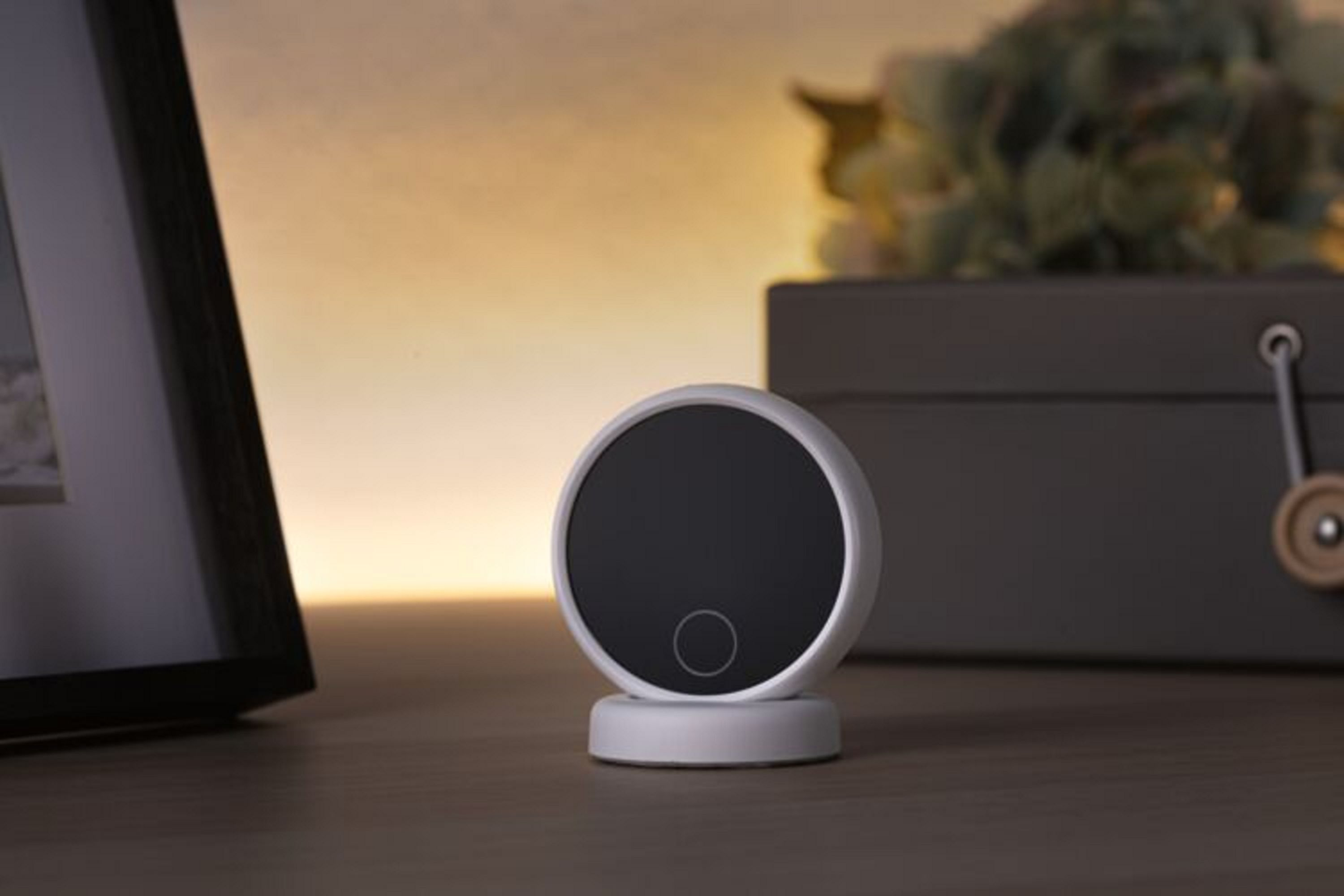 Małe, białe, okrągłe urządzenie na stojaku. Znajduje się na stole z ciemną ramą i elementem dekoracyjnym.