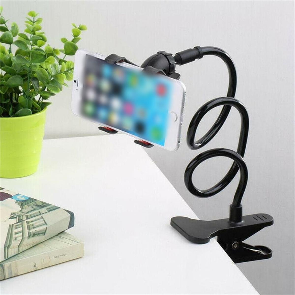 Ein Telefon wird in einem flexiblen schwarzen Telefonhalter an einem Tisch befestigt. Eine grüne Pflanze befindet sich in der Nähe.