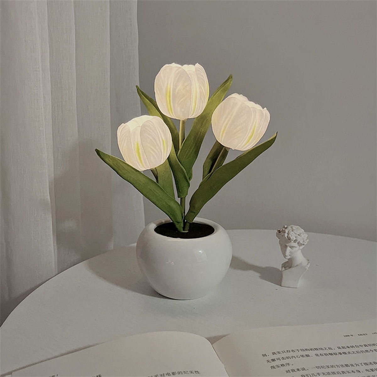 Eine weiße Vase mit drei weißen tulpenförmigen Lichtern und einer kleinen weißen Statue.