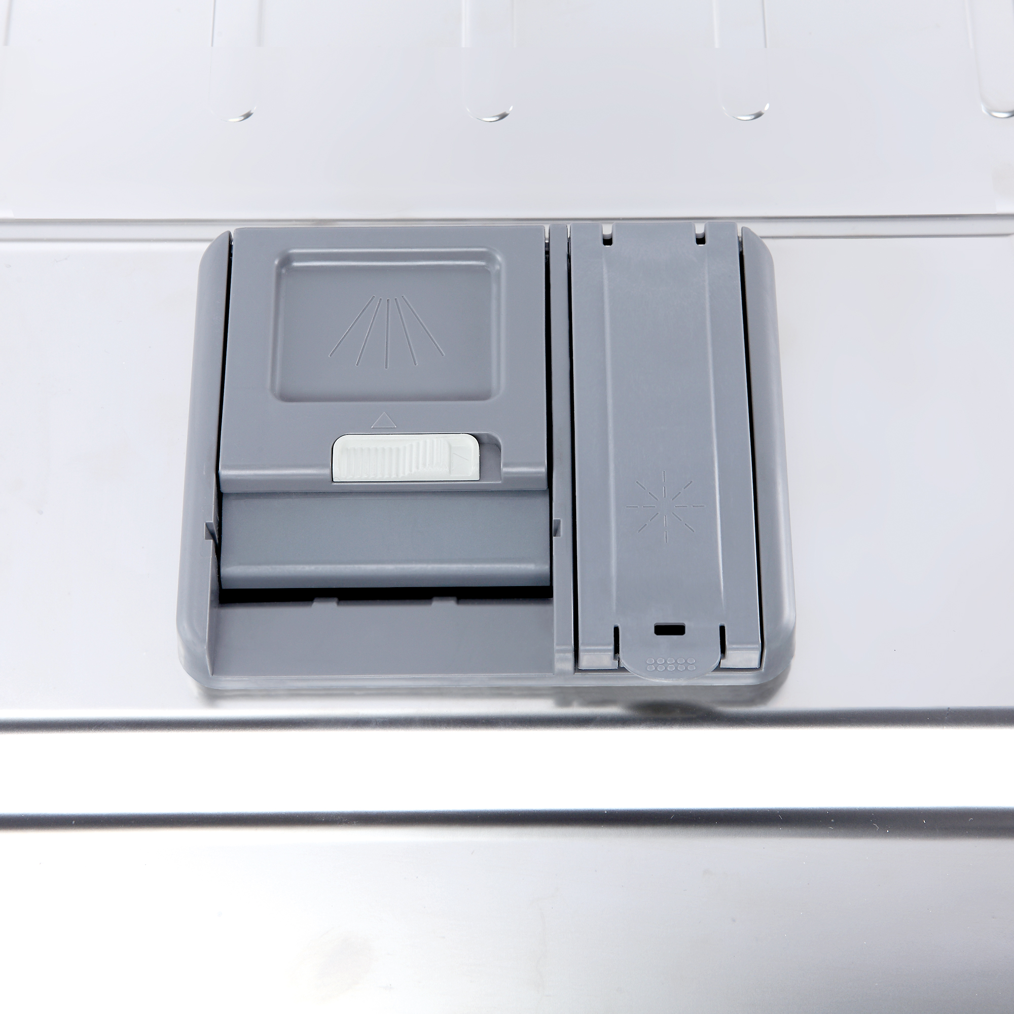 Primer plano del dispensador de jabón del lavavajillas. El dispensador es gris y metálico.