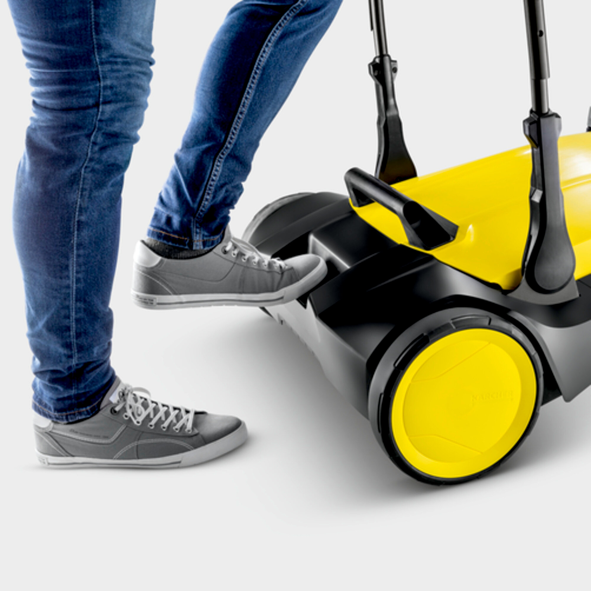 Person tritt auf eine gelb-schwarze Straßenkehrmaschine. Graue Schuhe sichtbar.