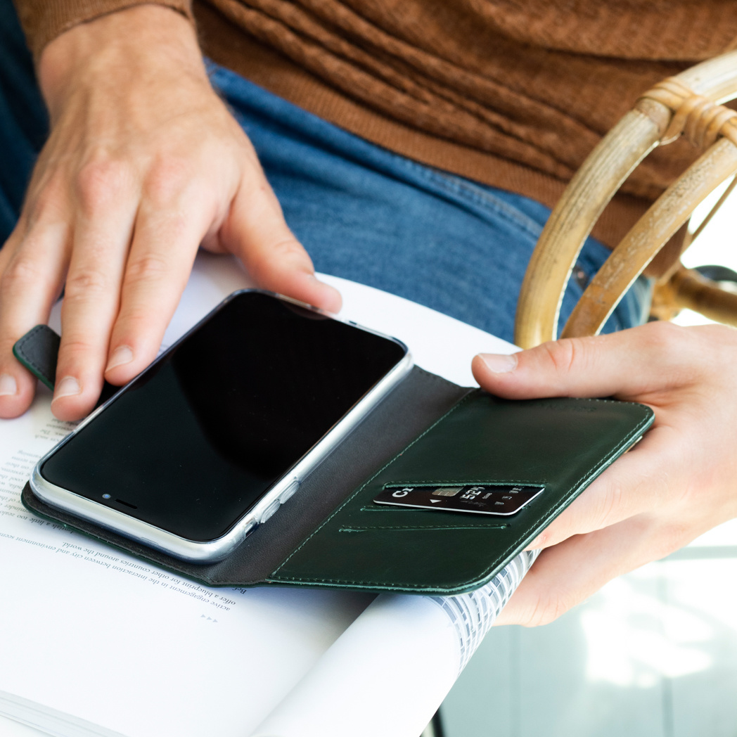 Handen houden een open, groene telefoonhoes vast. Binnenin zitten een telefoon en een kaart. De achtergrond is een pagina tekst.