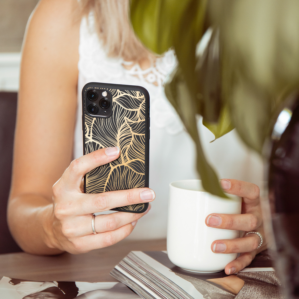 Vrouw die telefoon met gouden hoesje, een witte beker en plant vasthoudt.