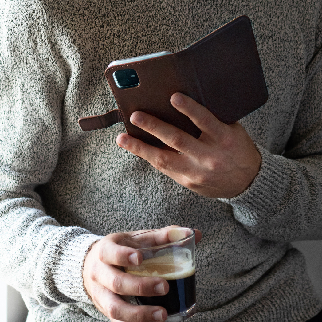 Une personne tenant un étui de téléphone et un verre de liquide sombre, probablement du café.