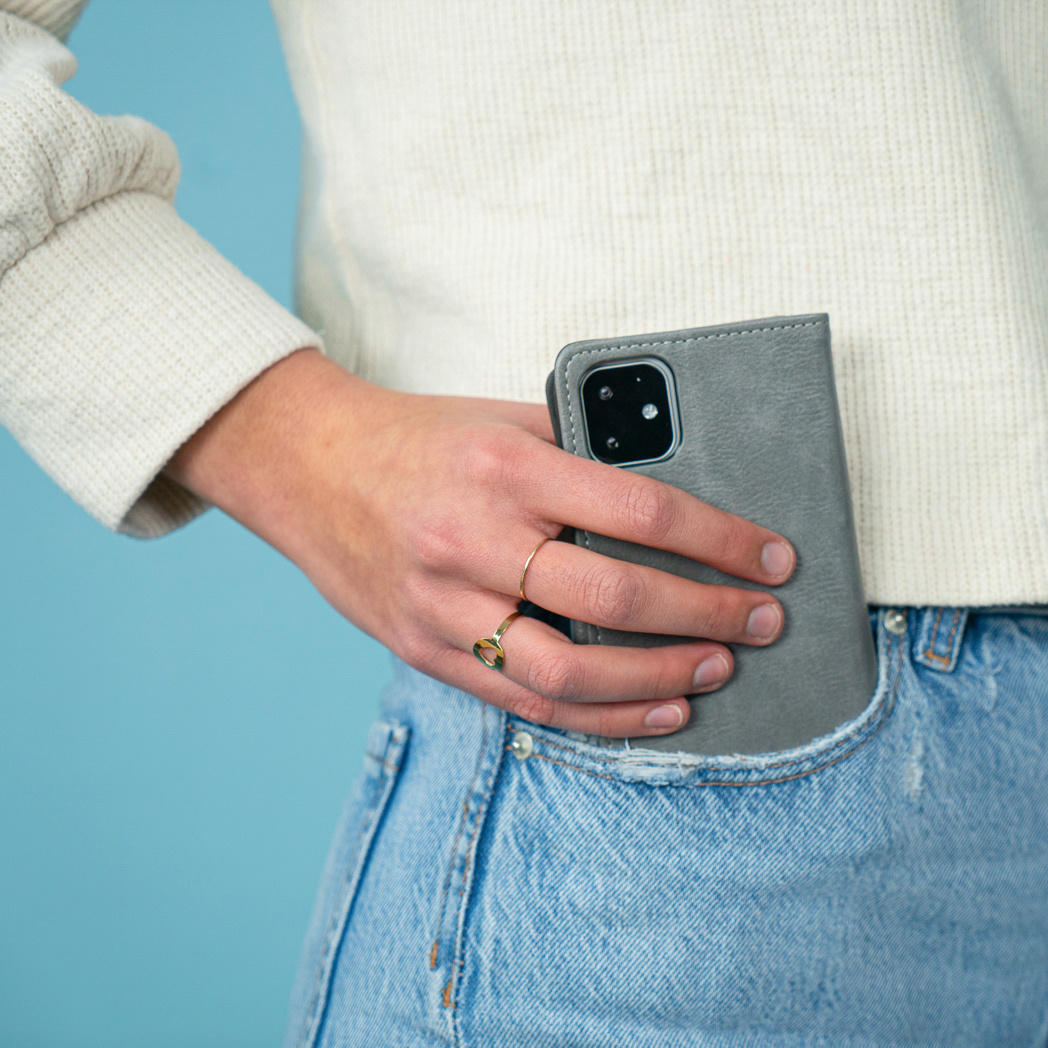 De hand van een persoon in een jeanszak met een grijze telefoonhoes.