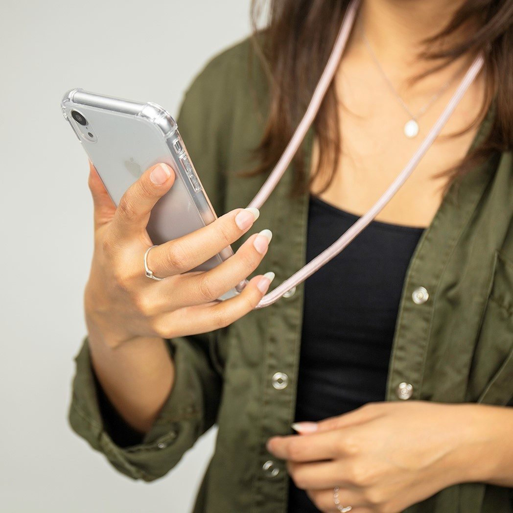 Vrouw die een doorzichtige telefoonhoes met telefoon vasthoudt, draagt een olijfgroene jas en een ketting.