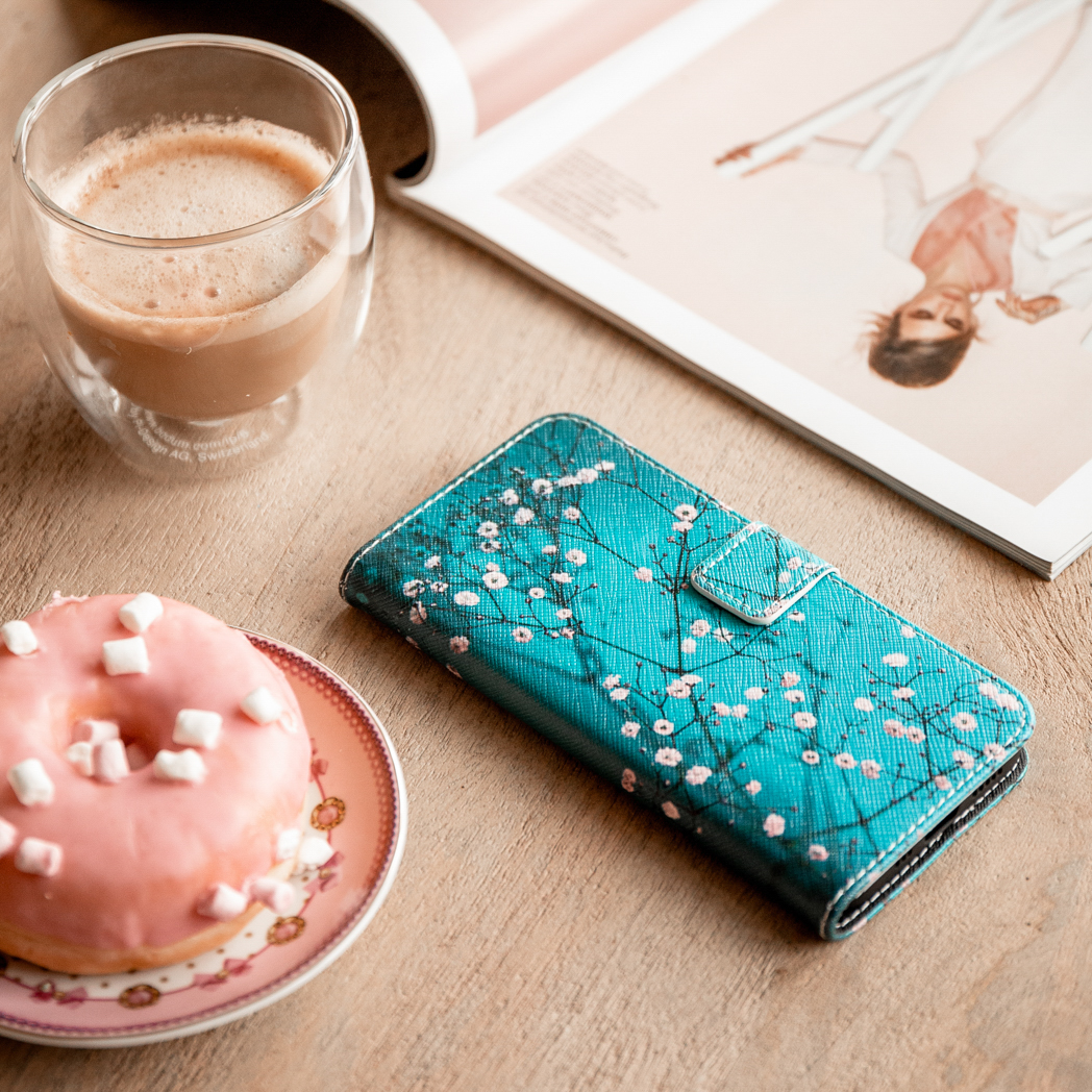 Un étui de téléphone avec un design floral, un donut sur une assiette, café, un magazine.