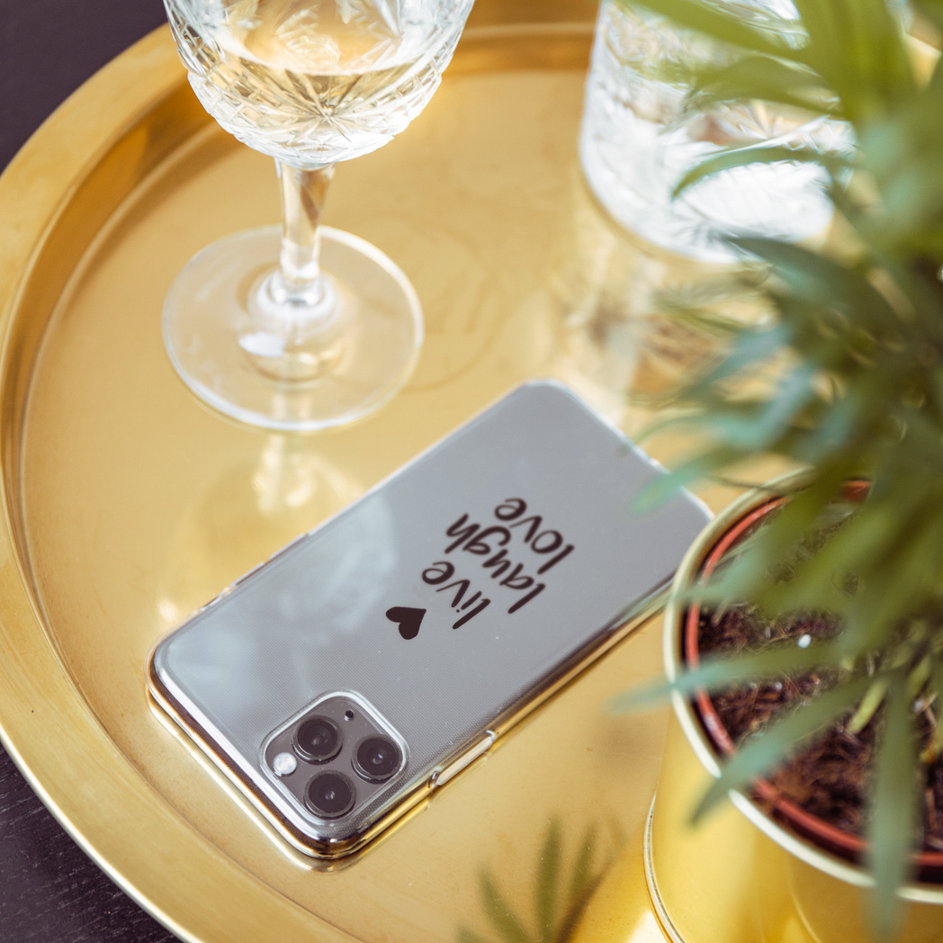 Telefoon op gouden dienblad, wijnglas, plant. Telefoon: 'Leef, Lach, Lief'.