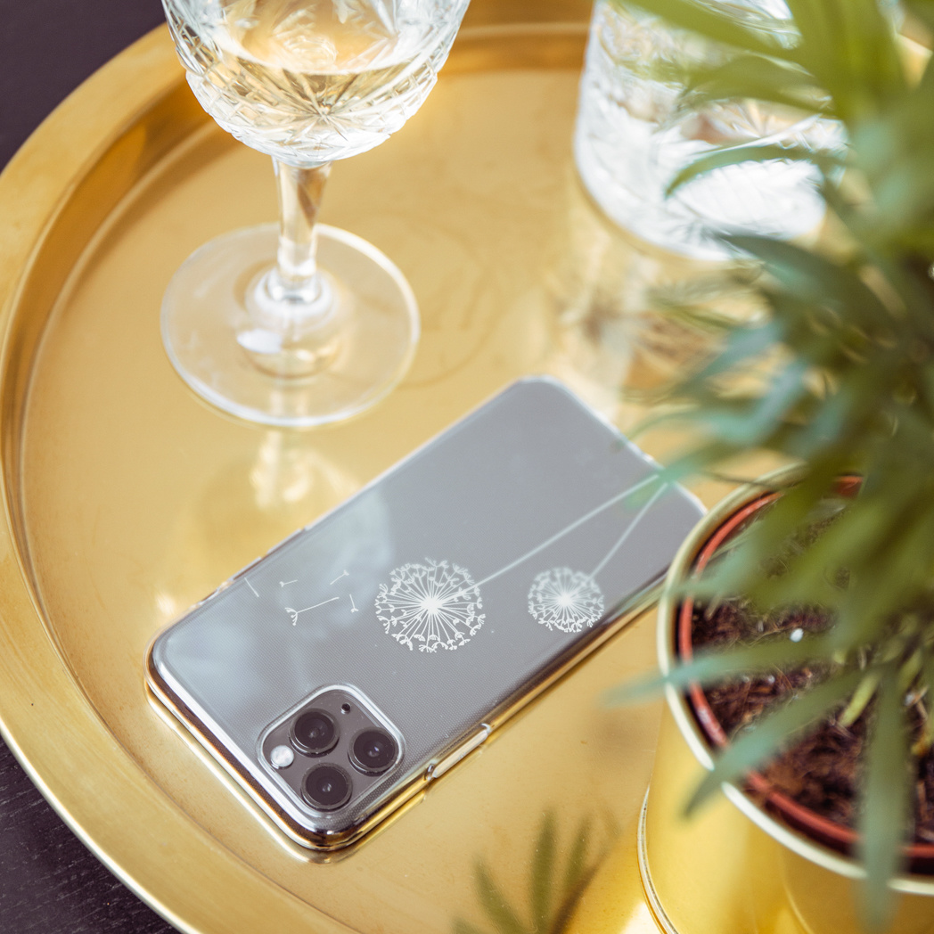 Téléphone sur un plateau doré avec un verre à vin et une plante. L'étui du téléphone a un motif de pissenlit.