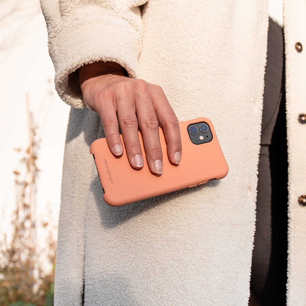 Een hand die een oranje telefoonhoes vasthoudt, tegen een witte jas.