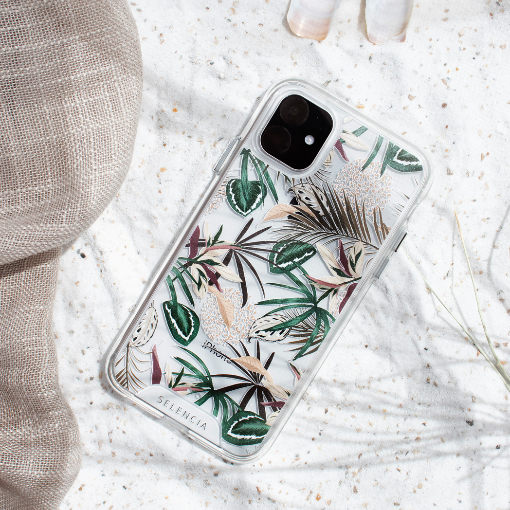 Une coque de téléphone avec un motif floral est posée sur une surface sablonneuse. Un tissu beige est à proximité.