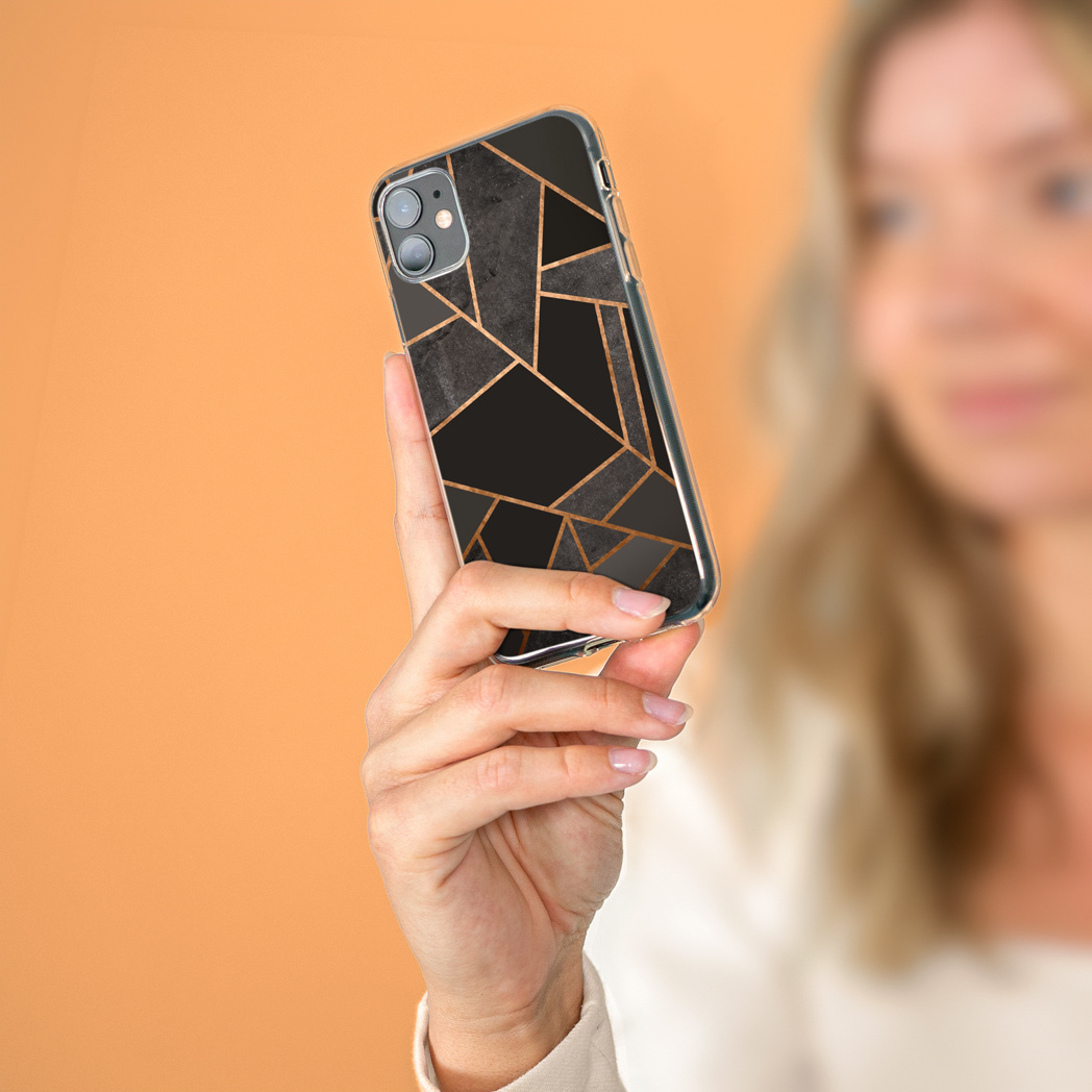 Een persoon houdt een telefoon vast met een zwart en goud geometrisch design hoesje, tegen een oranje vage achtergrond.