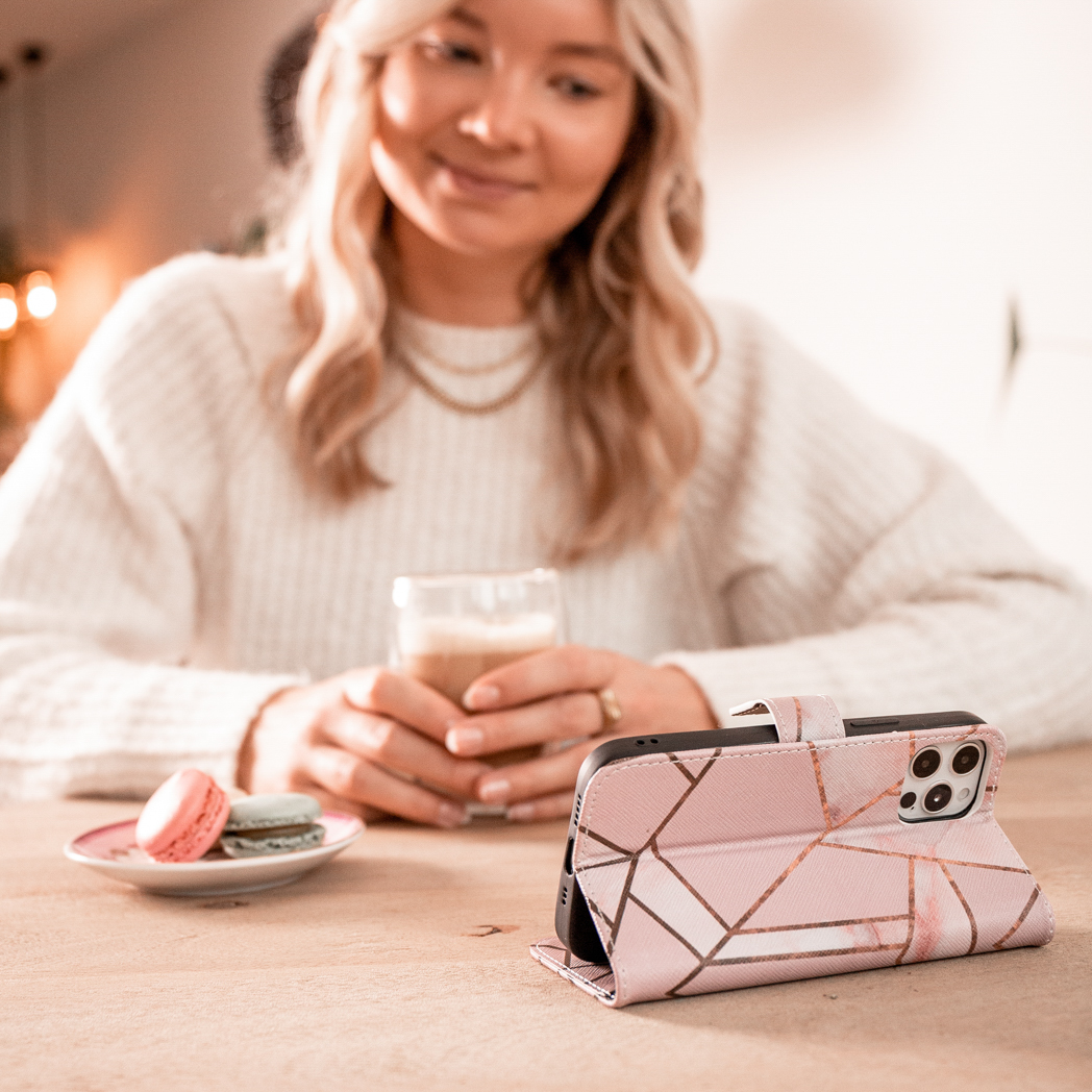 Femme blonde avec un étui de téléphone sur une table. Macarons et une tasse de café sont visibles.