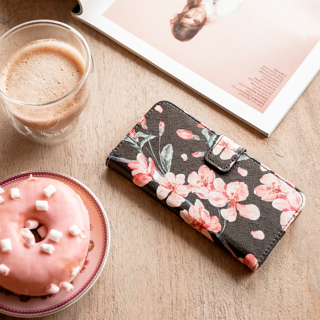 Telefoonhoesje met bloemenontwerp, koffie en roze donut op houten tafel.