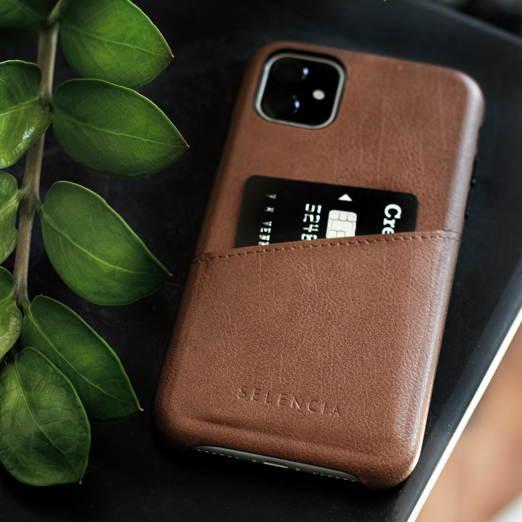 Un étui de téléphone marron avec une poche pour cartes. Une carte de crédit noire est insérée dans la poche. L'étui est sur un bureau.
