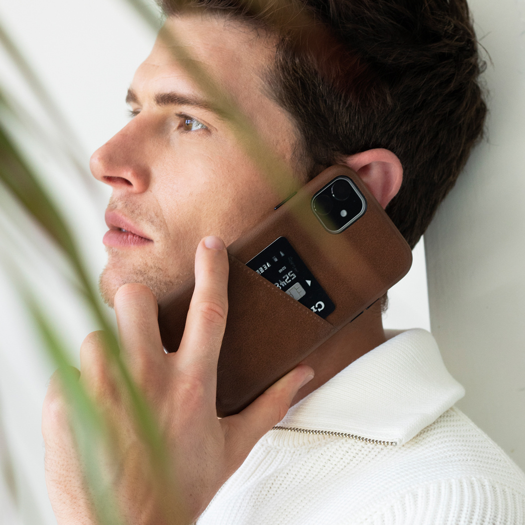 Un homme tenant une coque de téléphone marron avec des fentes pour cartes, appuyé contre un mur blanc.
