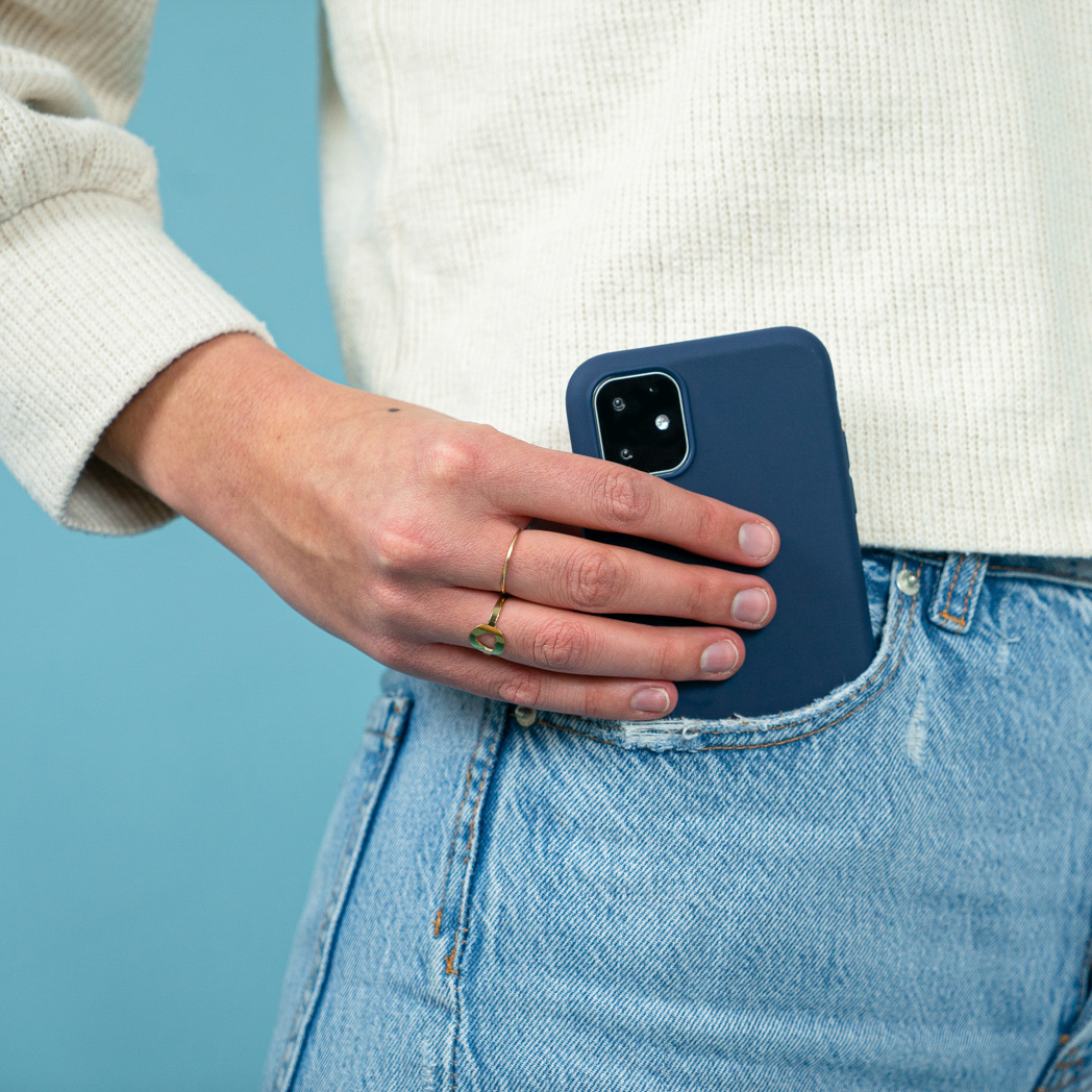 La main d'une personne dans une poche tenant un étui de téléphone bleu. L'étui protège un téléphone. Le fond est bleu.