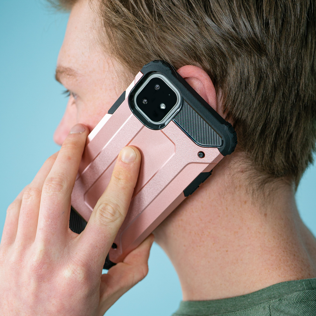 Een persoon die een telefoon aan zijn oor houdt. De telefoon is roze met een zwart accent en een zwart hoesje.