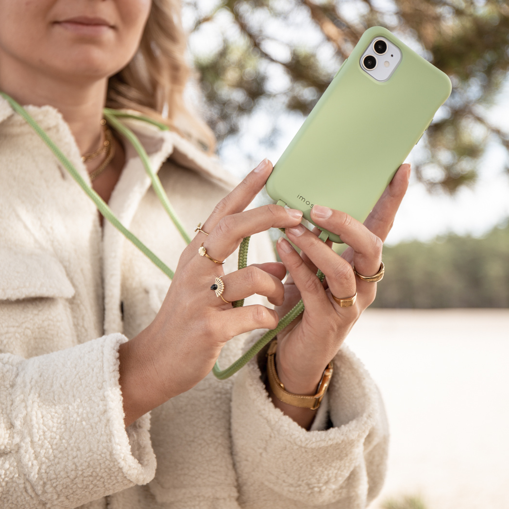 Vrouw met een lichtgroene telefoon met een groene band, draagt ringen en een witte jas.
