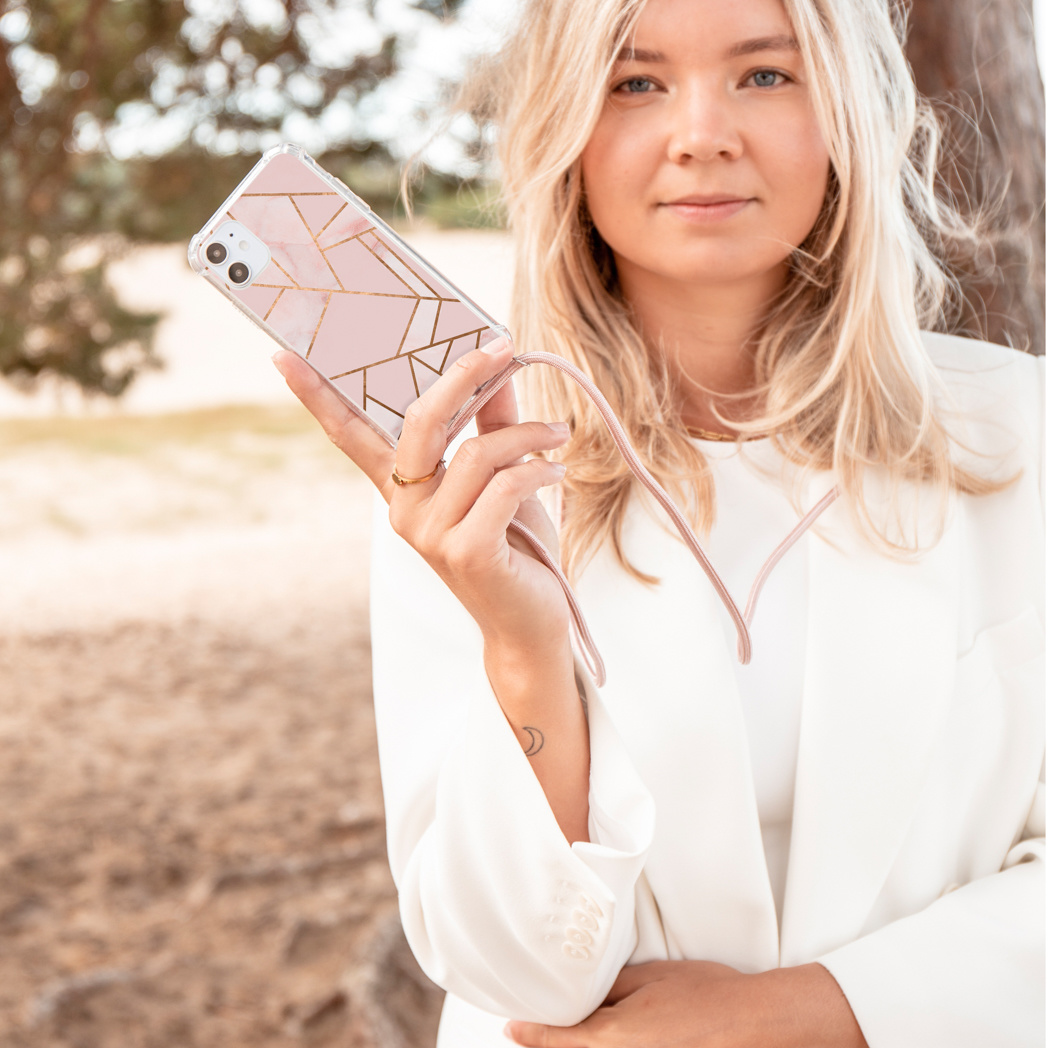 Vrouw in het wit houdt telefoon vast met een roze geometrische hoes en een roze band, buiten.